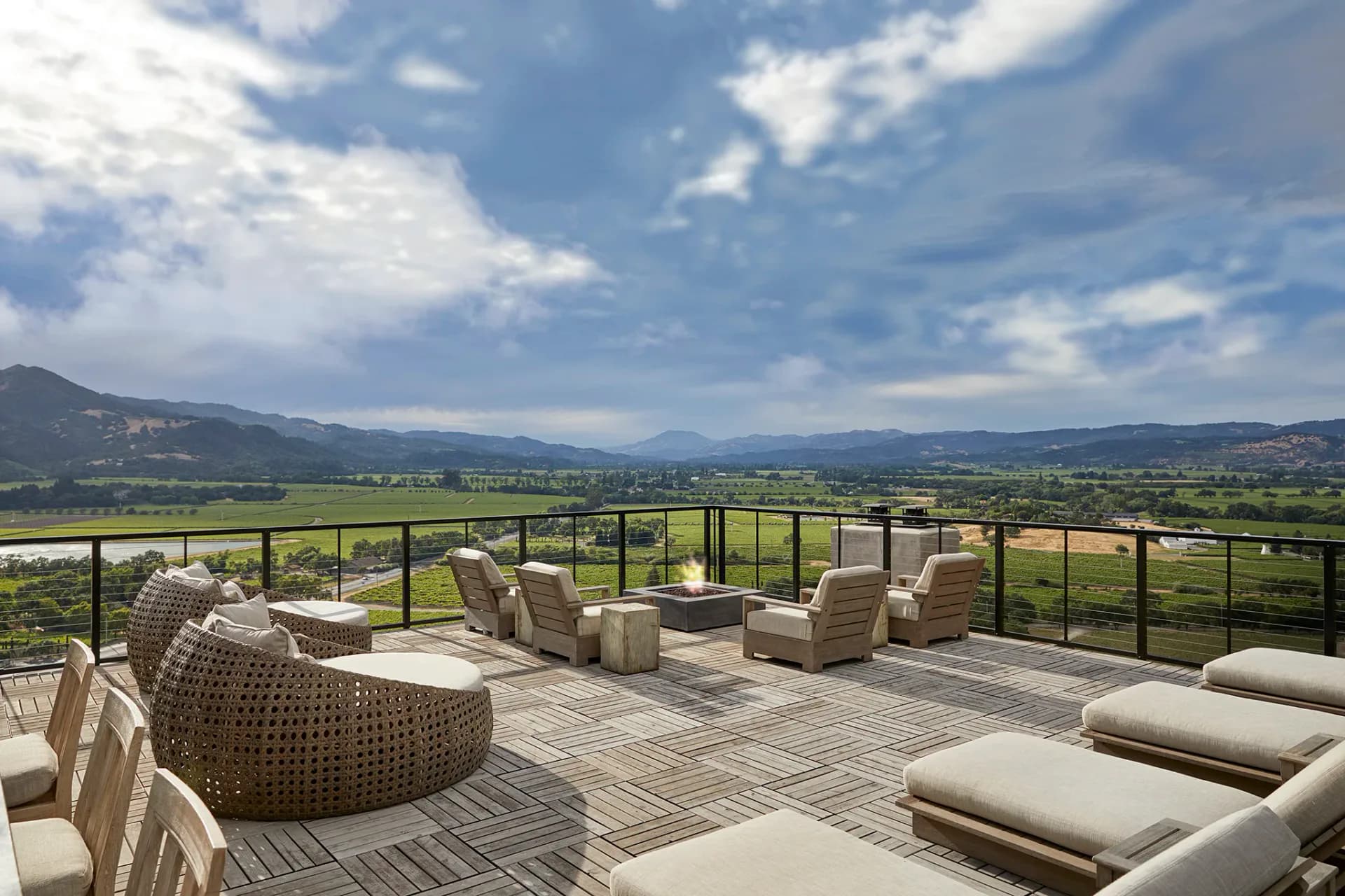 Modern terrace with woven lounge chairs, neutral cushions, and panoramic valley views, designed by Briana Kimball.