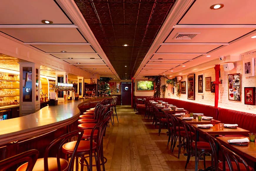 A warm-toned restaurant interior with burgundy banquettes, wooden floors, and ambient lighting throughout the elongated dining space by Brianna Alves.