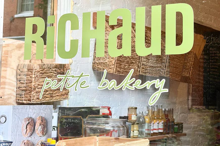 Storefront signage for Richaud Petite Bakery featuring large green lettering and a window display with baked goods and products by Brianna Alves.