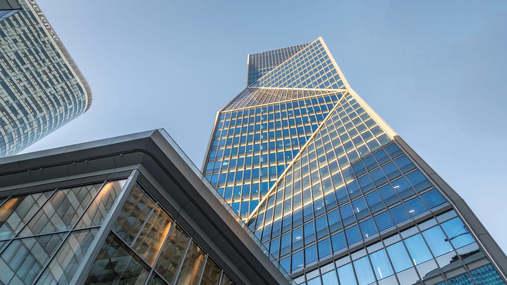 Modern skyscraper with reflective glass and steel facade photographed from below against clear blue sky, showcasing contemporary architectural design by Brittany Conner.