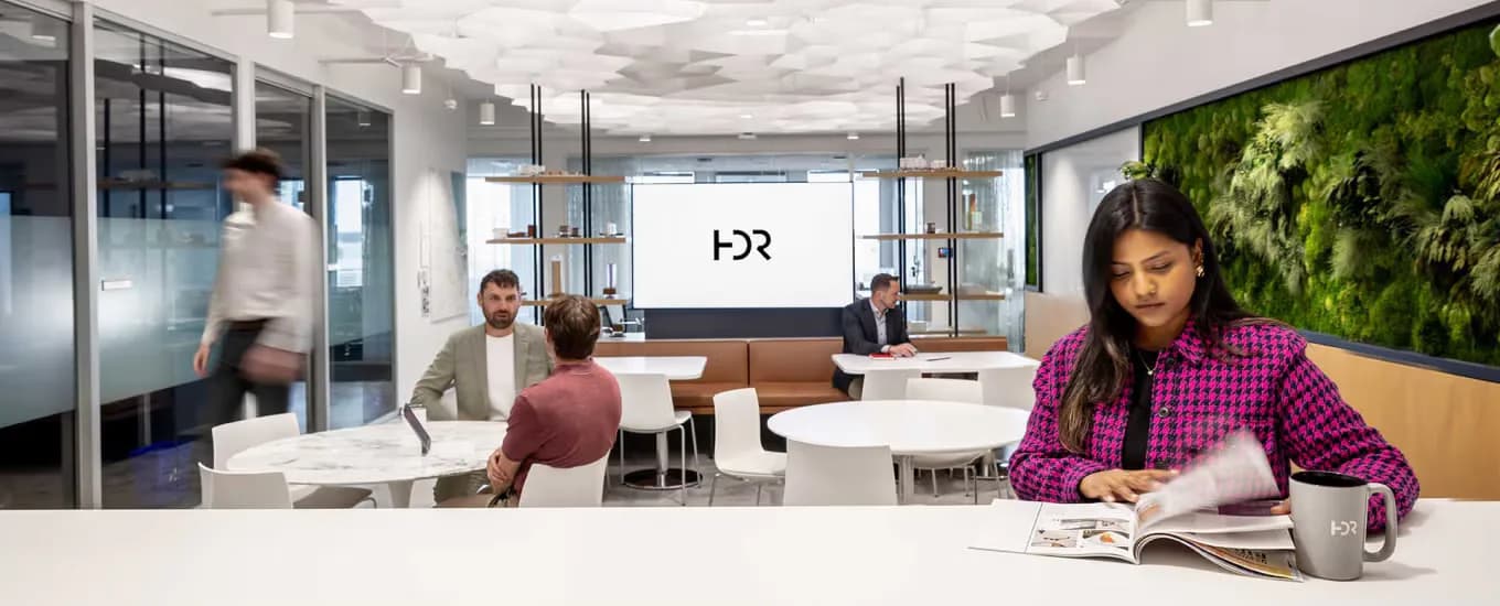 Modern office lounge with glass partitions, warm wood accents, green living wall, and collaborative seating areas designed by Brooke Horan.