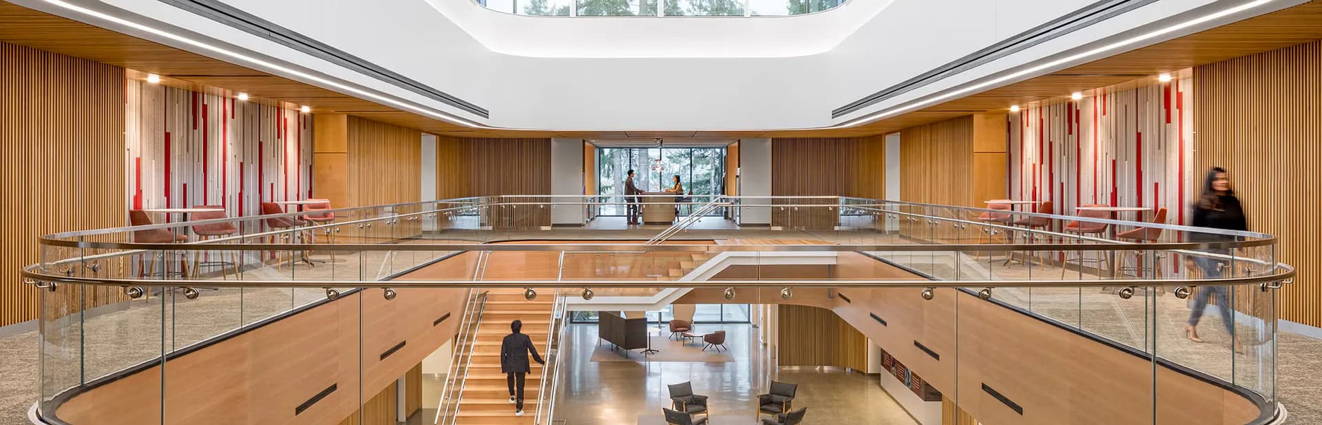 Modern multi-level interior with warm wood paneling, glass railings, and skylight by Brooke Horan.