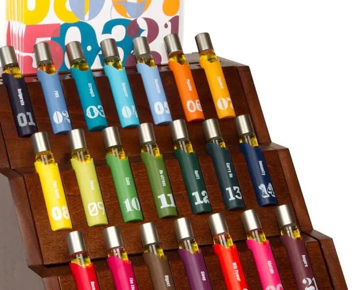 Wooden display stand featuring numbered bottles in a gradient color arrangement from blue to red, designed by Bruce Teitelbaum.
