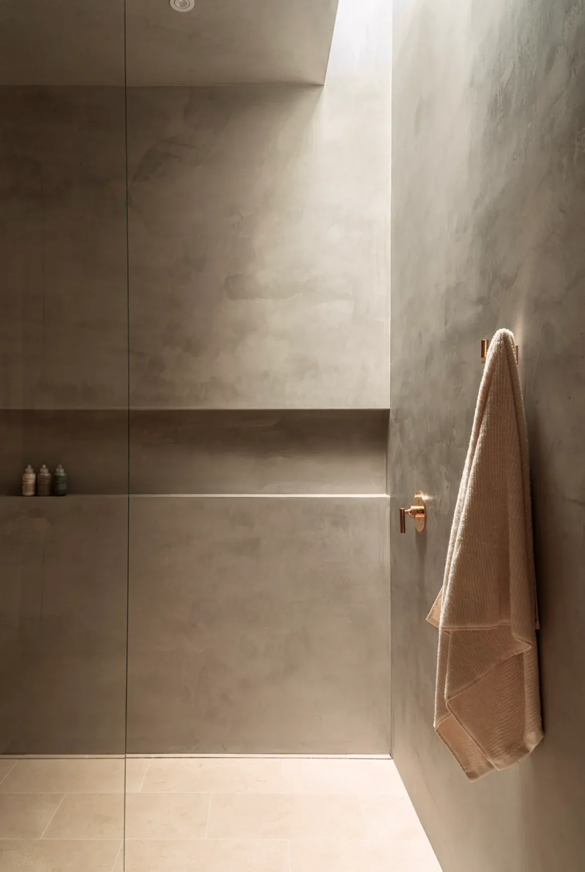 Minimalist bathroom with concrete walls, frameless glass shower enclosure, and beige towel by Burcu K.
