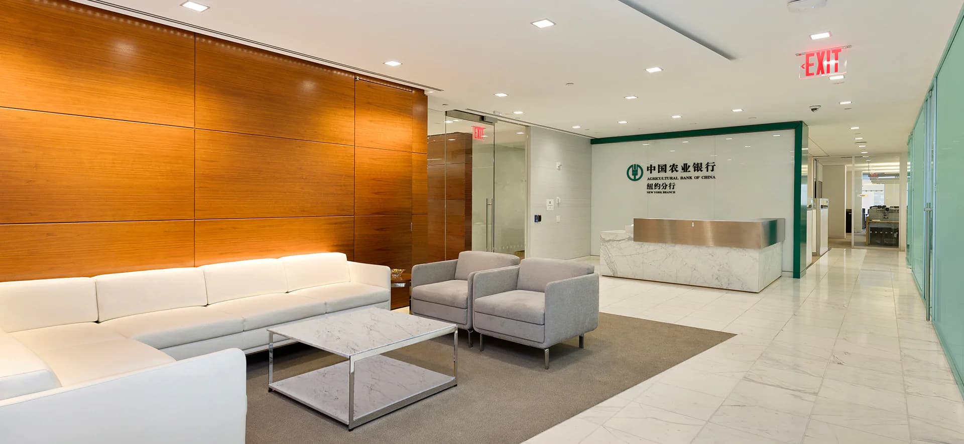Modern corporate lobby featuring warm orange wood-paneled walls, white seating area with gray accents, polished floor, and branded reception desk, designed by Carmelo Mazzaferro.