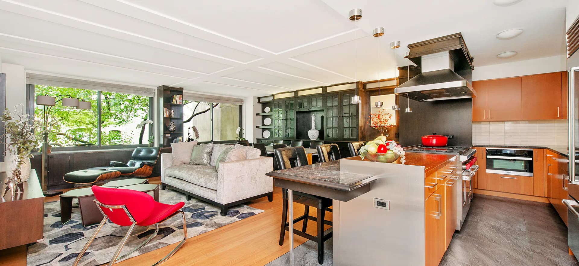 Open-plan kitchen and living area with orange cabinetry, gray island, cream sofa, and red accents by Carmelo Mazzaferro.