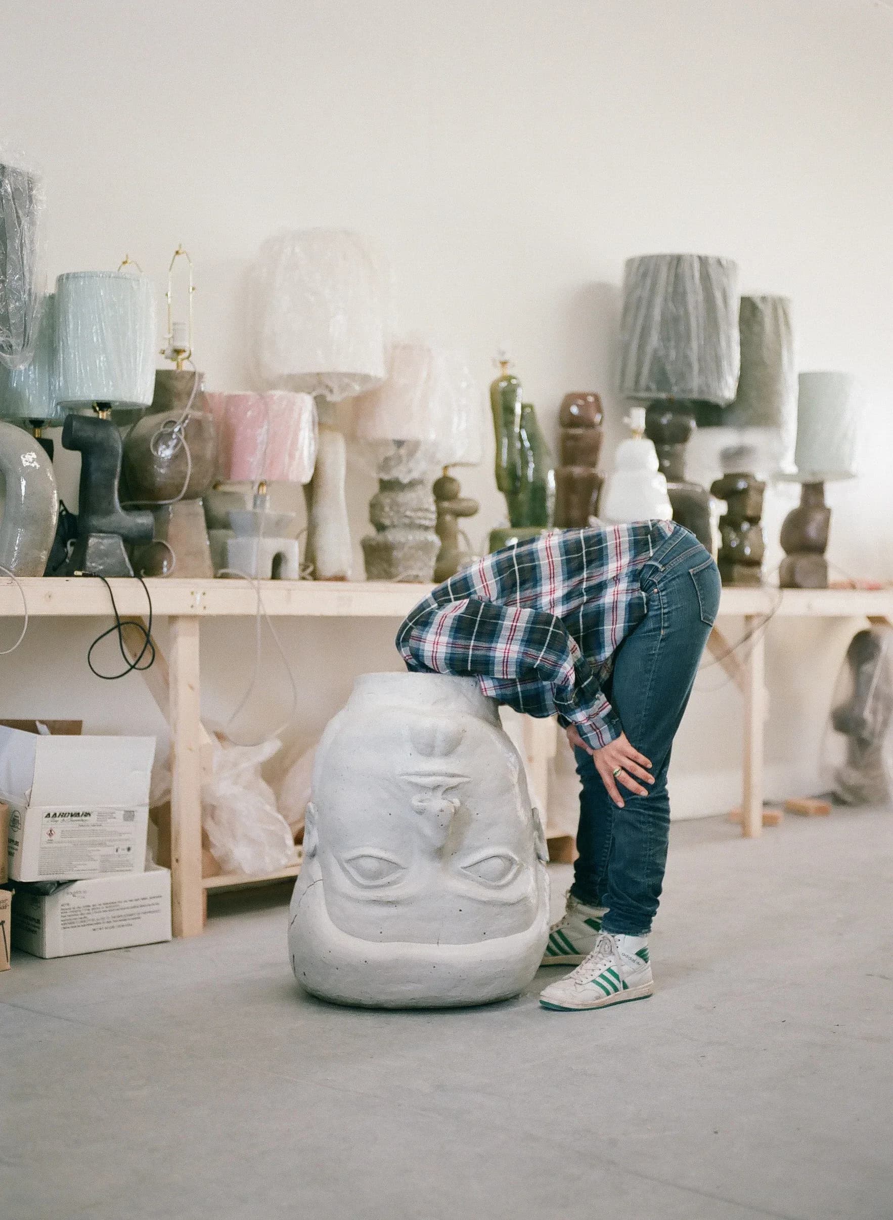 Artist's studio workspace with white plaster sculptural heads and busts displayed on shelves, featuring neutral palette and natural lighting by Carmen D'Apollonio.