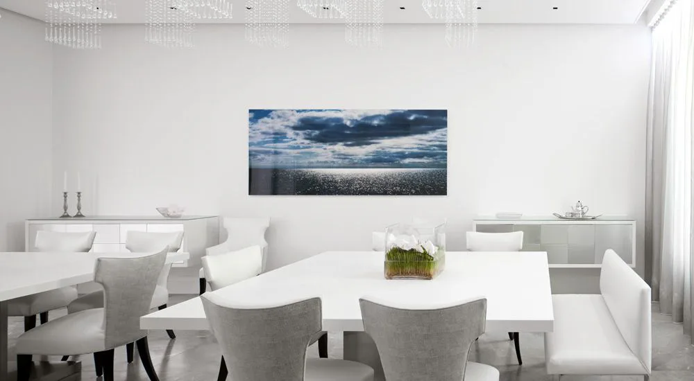 Modern dining room with white furnishings, gray upholstered chairs, and a landscape artwork above a built-in bench by Carol Brewer.
