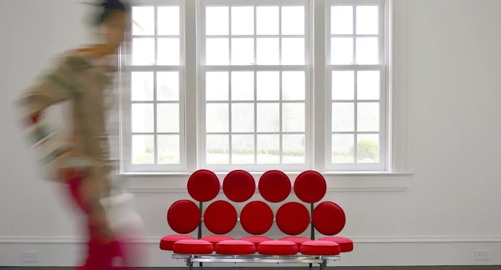 Modern interior with red spherical sculptural installation on platform in front of large gridded windows, by Carol Kurth.