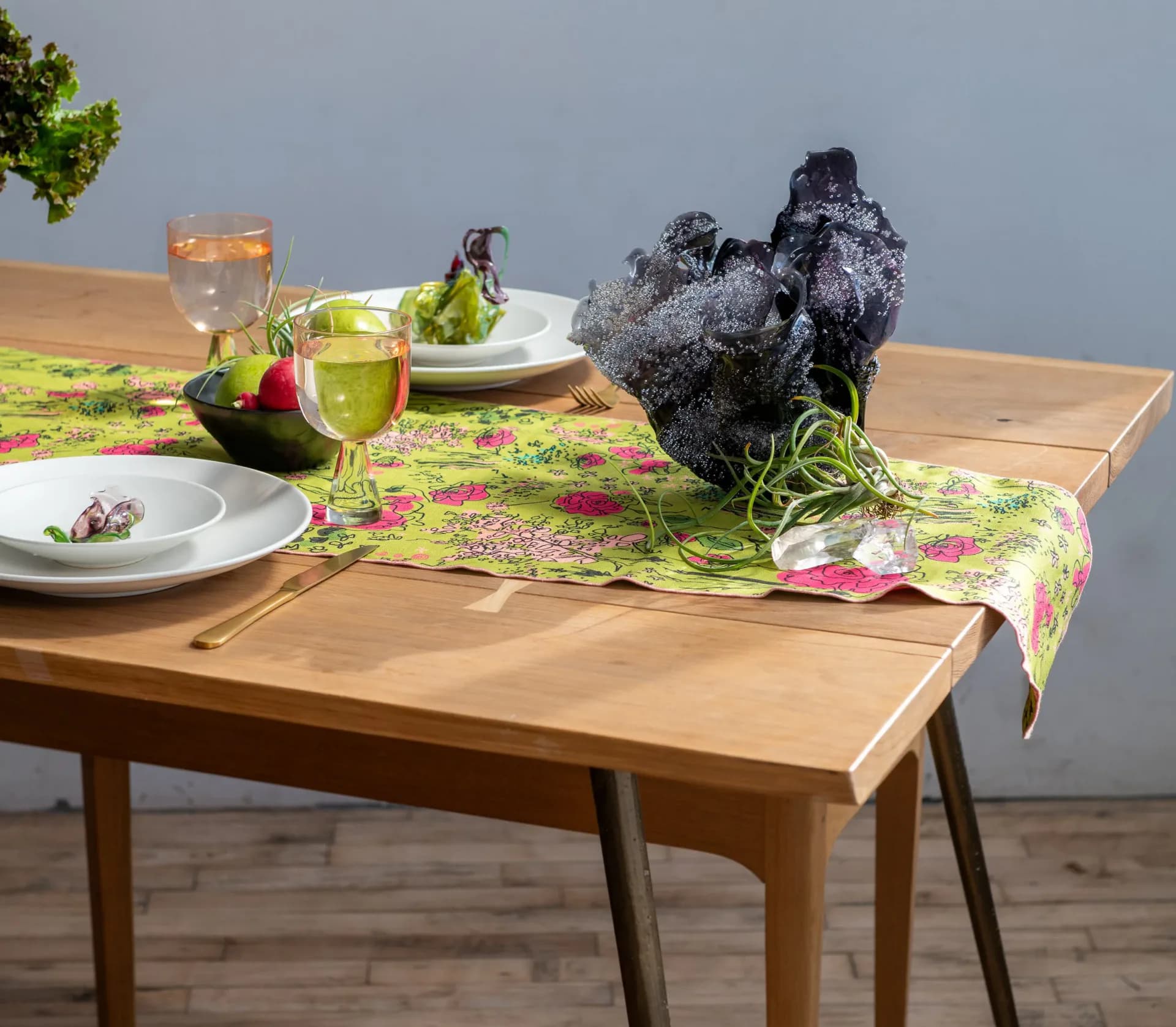 Styled table setting with wooden mid-century furniture, lime-green patterned runner, white plates, and decorative black sculptural elements by Caroline Zimbalist.