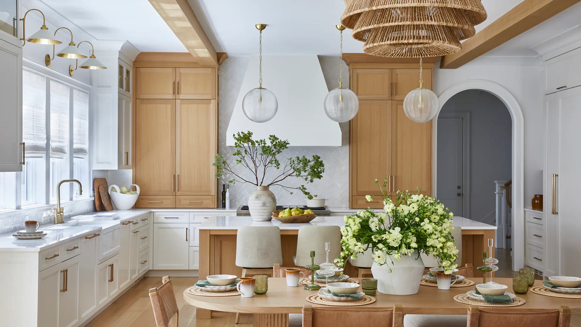 Bright, modern kitchen with natural wood cabinetry, white countertops, and a central wooden dining table styled with fresh florals and table settings by Caroline Zogheb.