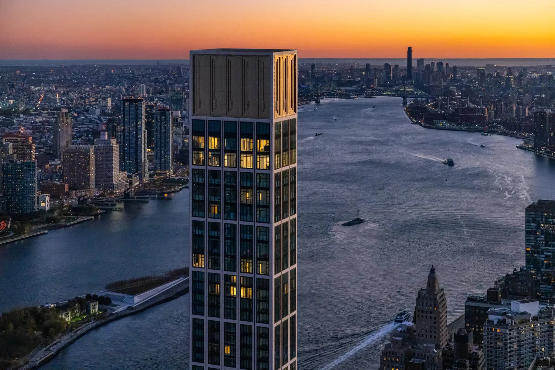Illuminated tall residential tower at sunset overlooking Manhattan's East River and skyline, designed by Cate Osborne.