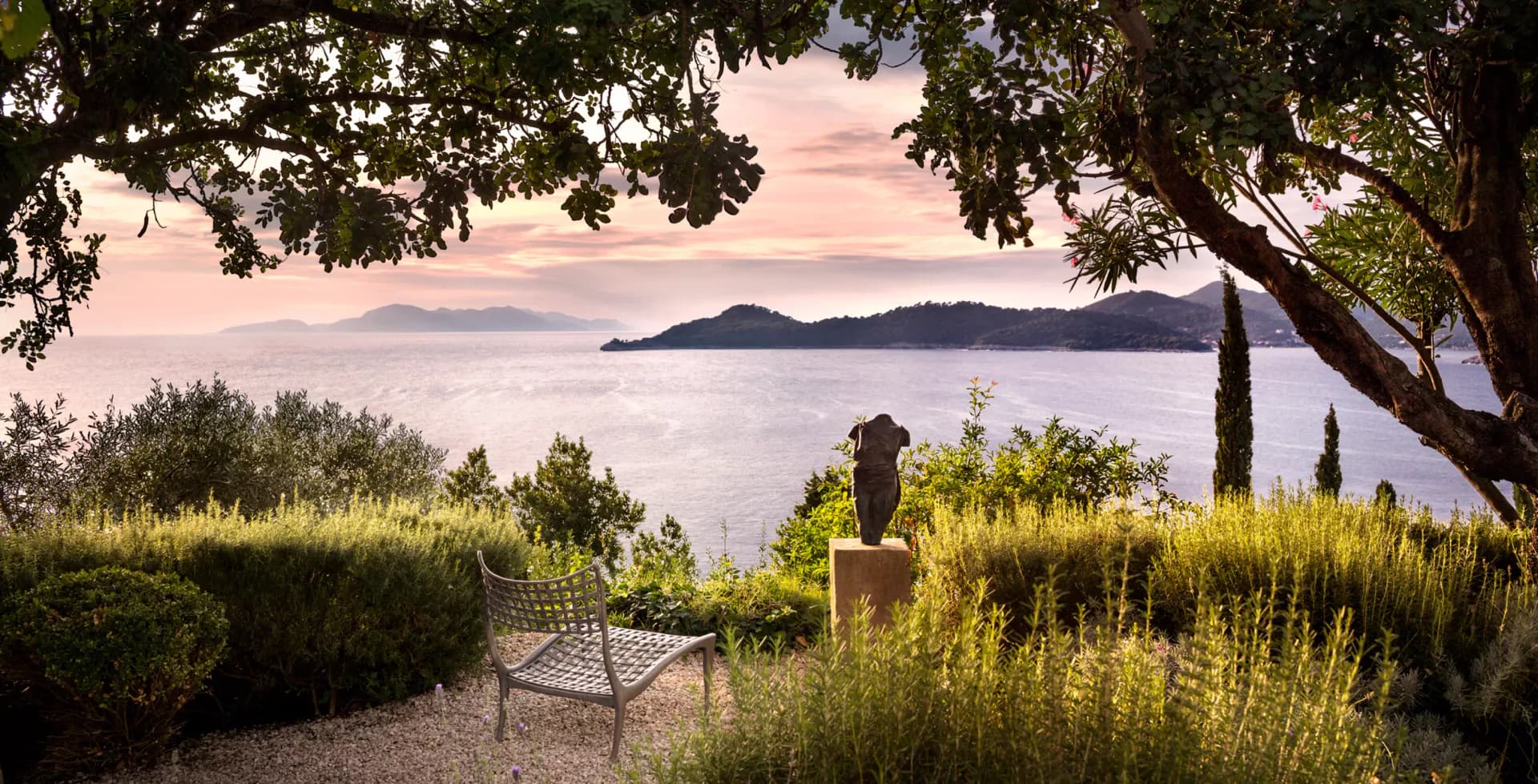 Coastal Mediterranean garden with stone bench, cypress trees, and sea view, designed by Cate Steinacker.