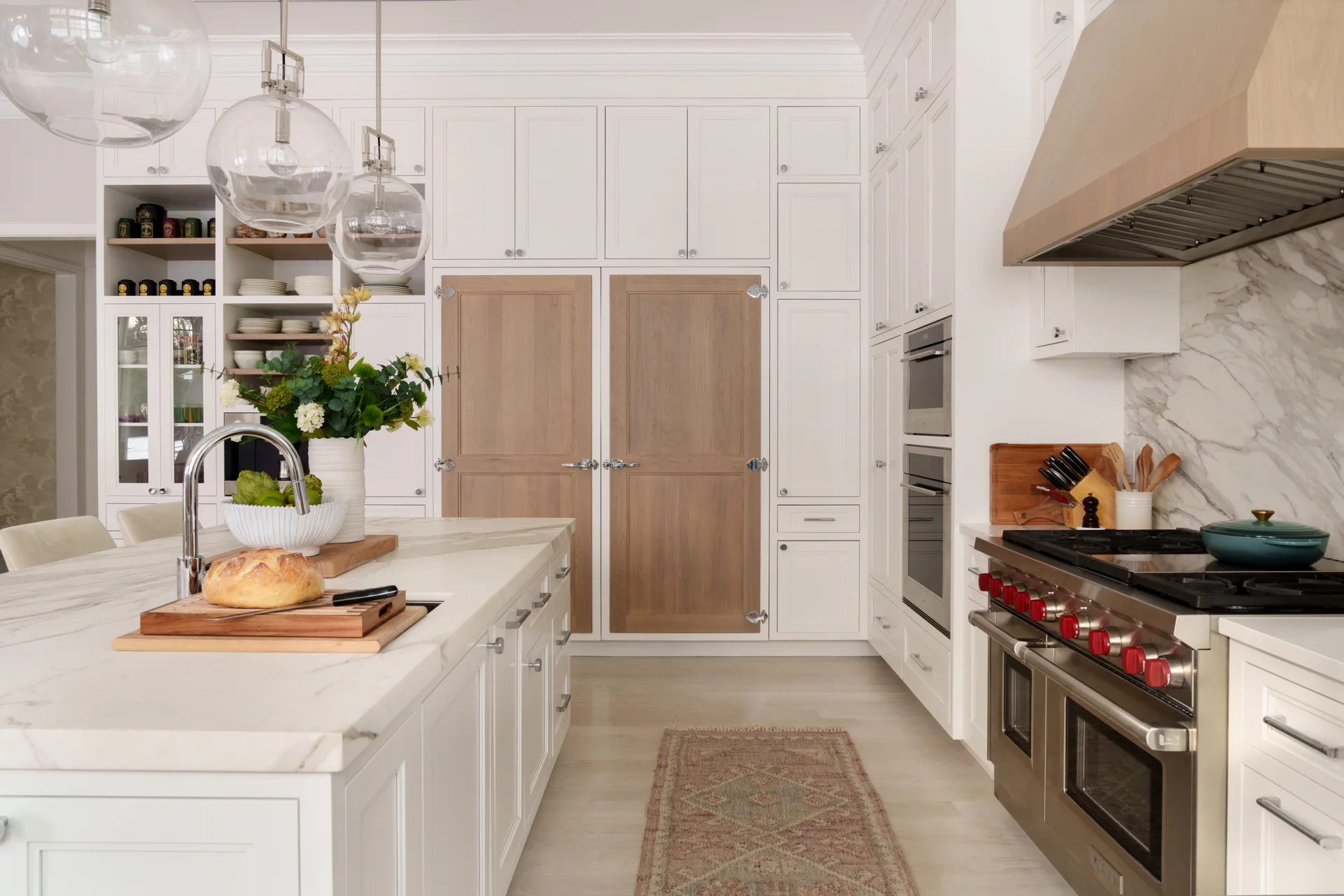 Contemporary kitchen with white cabinetry, marble countertops, stainless steel range, and wood-grain refrigerator panels, designed by Cecile Mattei Ekstrom.