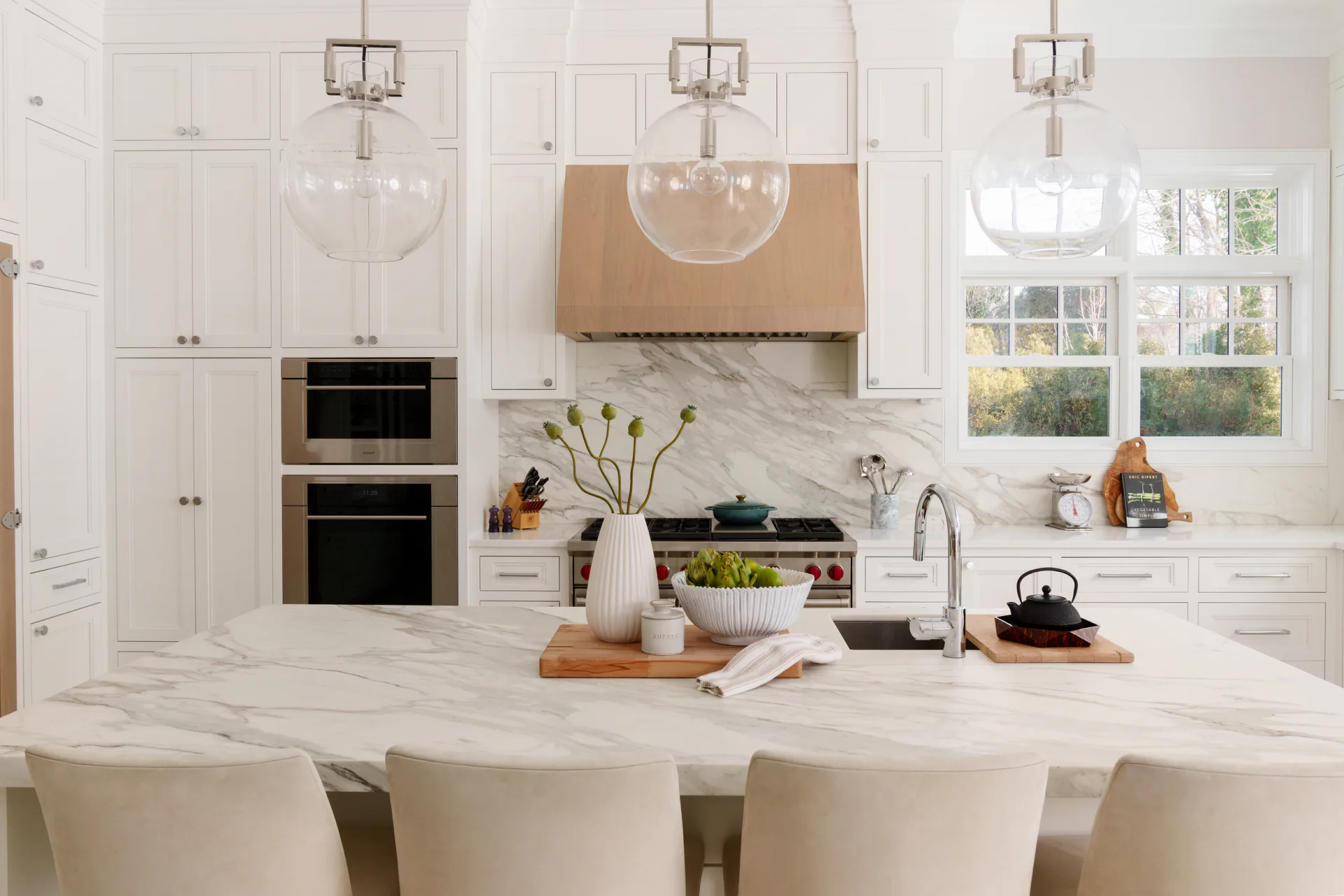 Bright white kitchen with marble countertops, waterfall island, custom cabinetry, integrated appliances, and pendant lighting designed by Cecile Mattei Ekstrom.