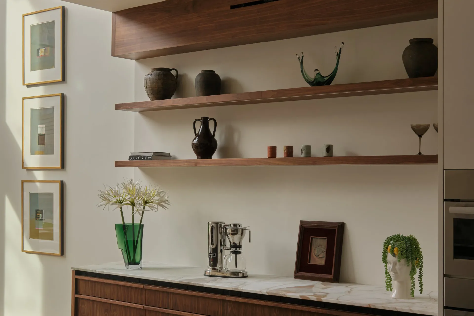 Modern kitchen shelving display with dark wood floating shelves, ceramic vessels, and decorative objects against a neutral wall, designed by Cem Evirgen.
