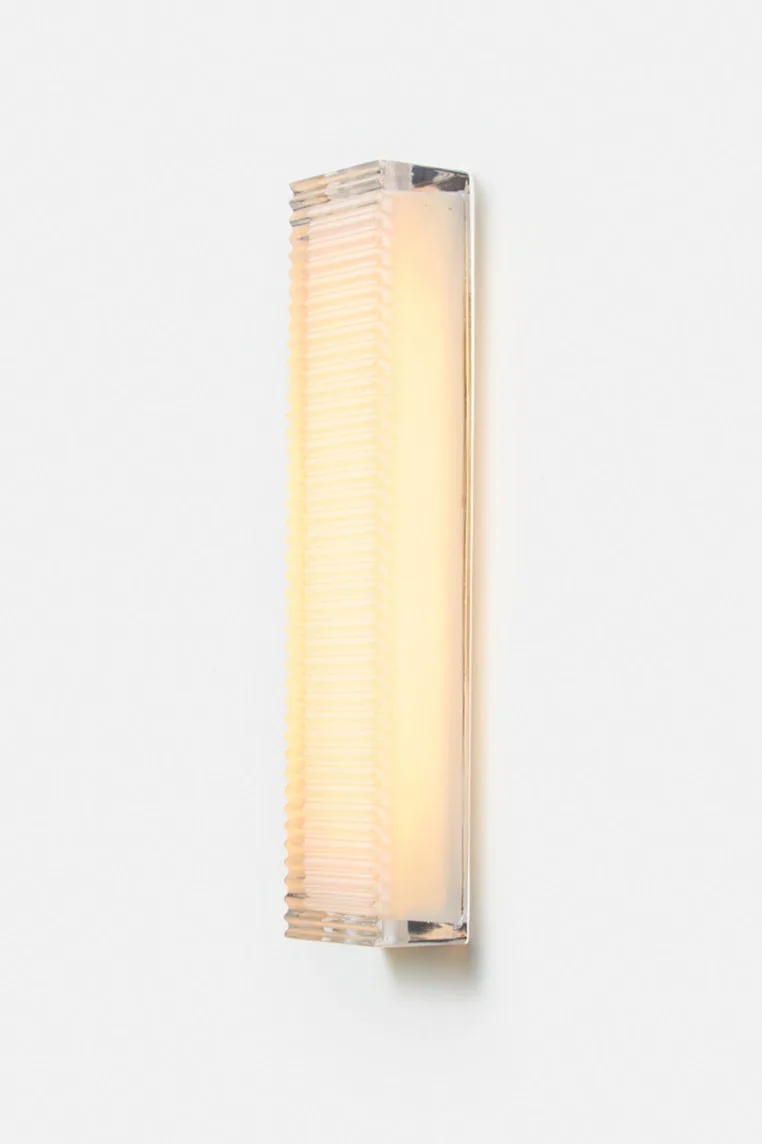 Tall vertical wall-mounted lighting fixture with ribbed frosted glass diffuser and polished metal mounting hardware, emitting warm light by Charles Brill.