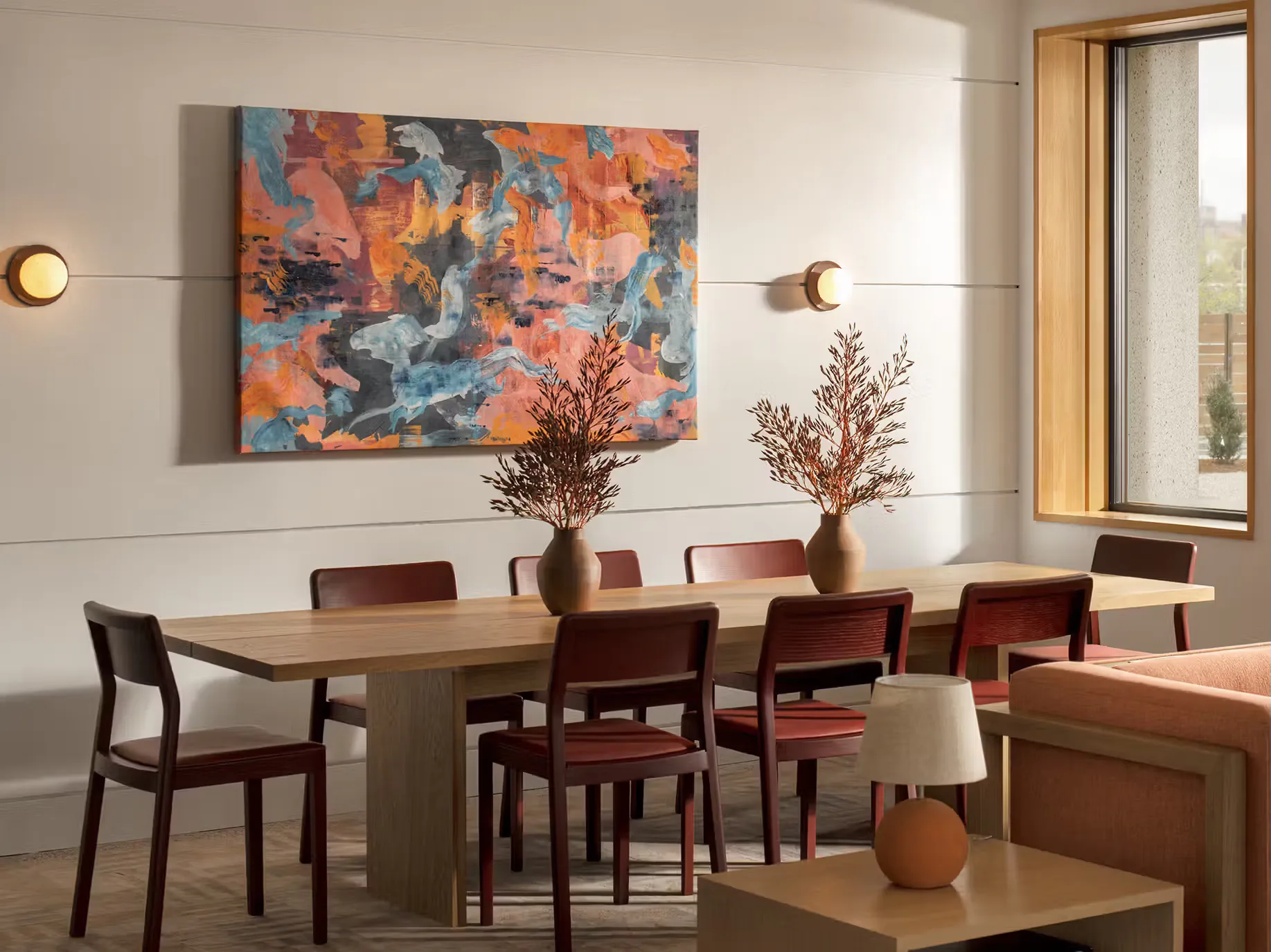 Modern dining room with wooden table, burgundy chairs, abstract orange and blue artwork, and decorative ceramic vessels by Charles Brill.