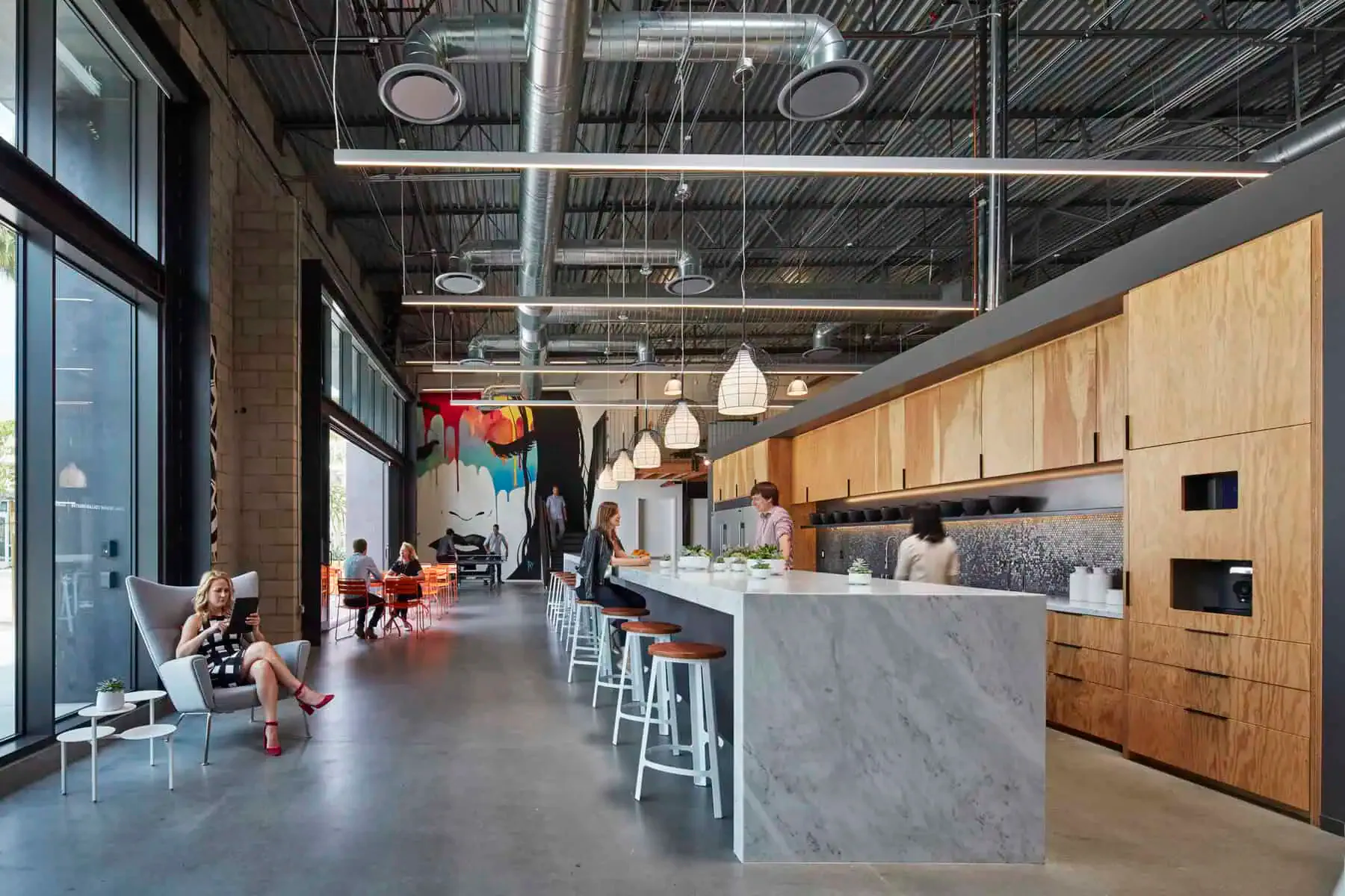Modern commercial kitchen and dining space with concrete flooring, light wood cabinetry, gray marble island counter, pendant lighting, and industrial ceiling details by Chaya Juntara.