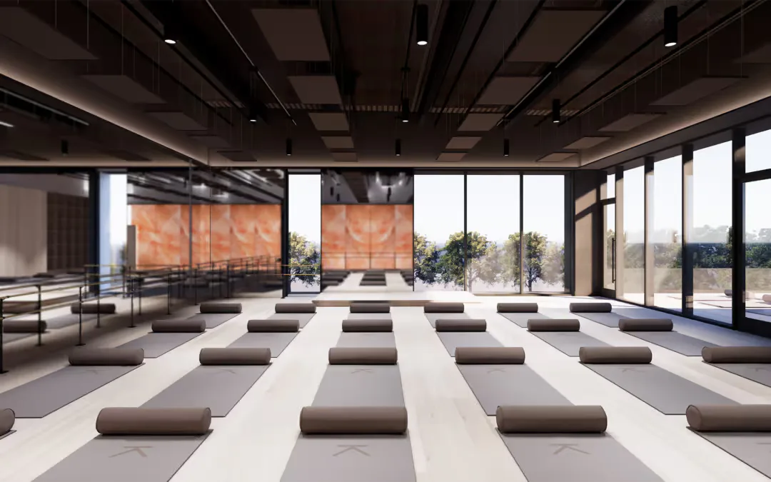 Modern yoga or meditation studio with striped flooring, brown cushions arranged in rows, floor-to-ceiling windows, and suspended orange panels by Chaya Juntara.