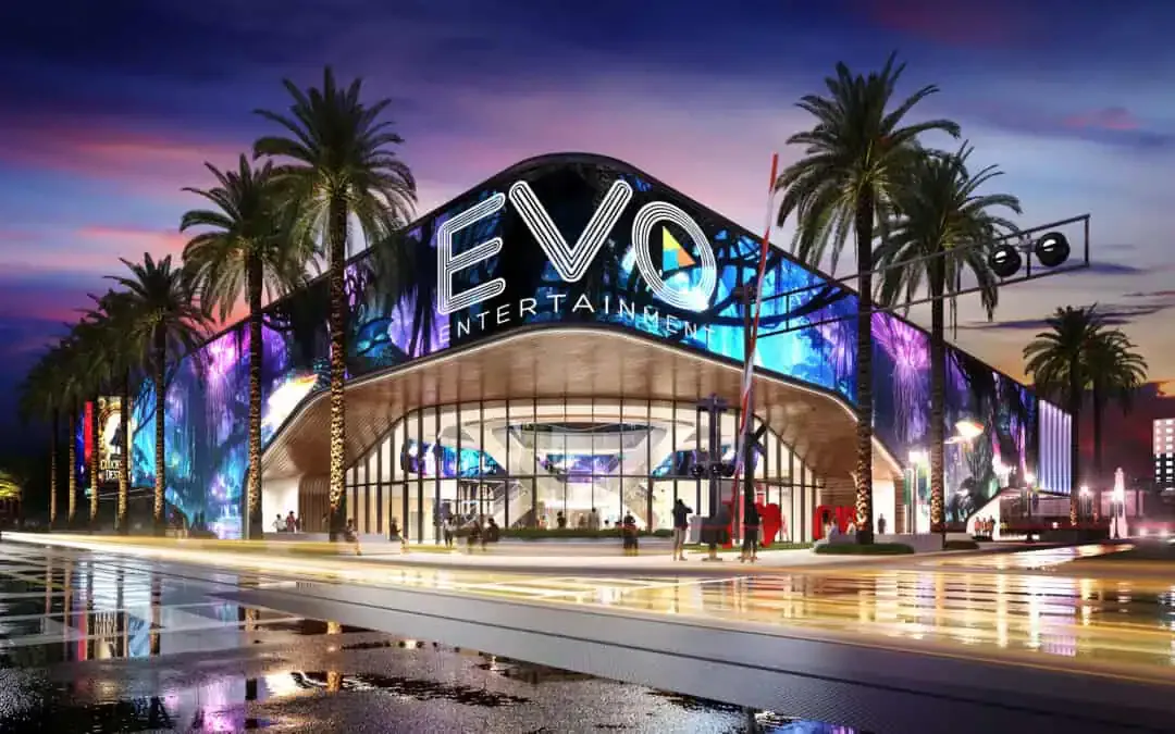Illuminated modern entertainment venue with curved digital facade, palm trees, and reflective plaza at dusk by Chaya Juntara.