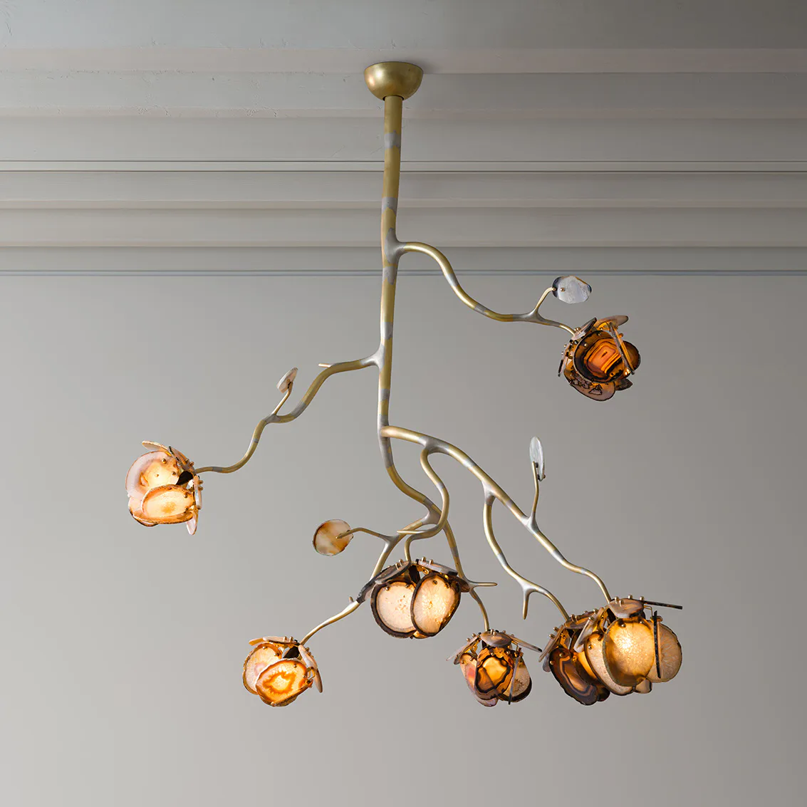 Brass chandelier with organic branching arms suspending amber glass globe pendants against a neutral ceiling by Chen Chen.