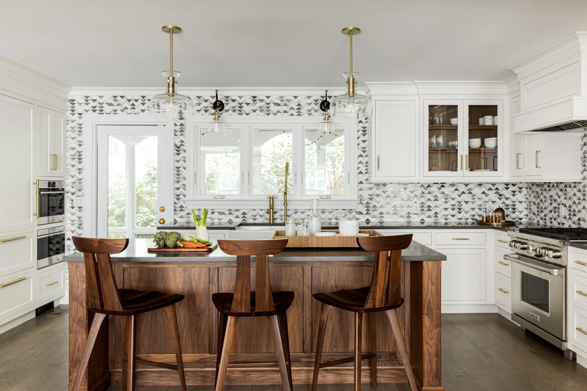 Modern white kitchen with mosaic tile backsplash, wood-topped island with bar seating, stainless steel appliances, and abundant natural light by Cherie Urrutia.
