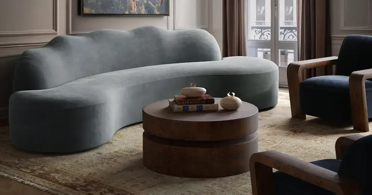 Modern living room with curved gray sofa, round wood coffee table, and wood-accented black chairs in neutral palette by Christiane Lemieux.