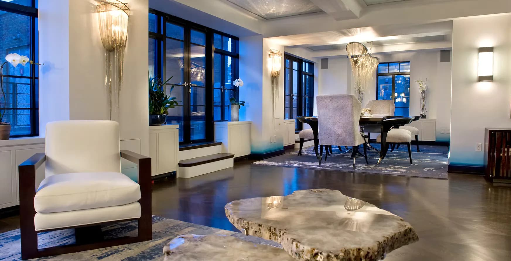 Modern lobby with polished concrete floors, cream armchair, sculptural stone table, and floor-to-ceiling windows by Christina Marraccini.