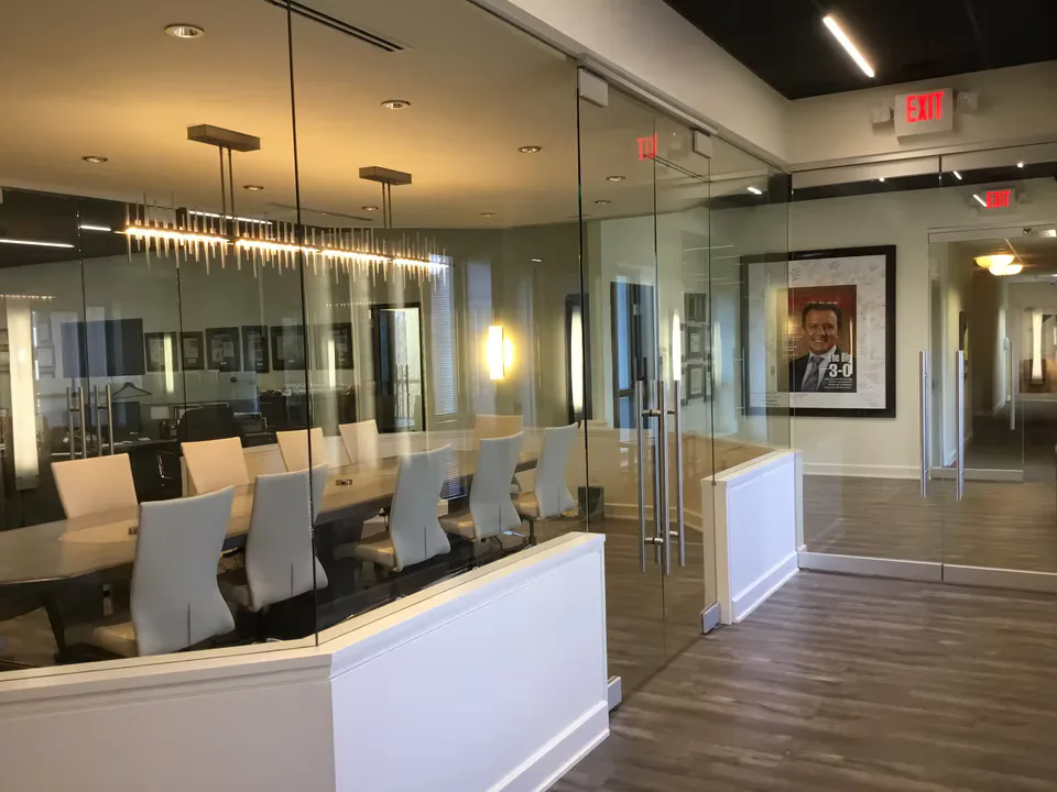 Modern office conference room with floor-to-ceiling glass walls, white cabinetry, wood flooring, and linear pendant lighting by Christina Marraccini.