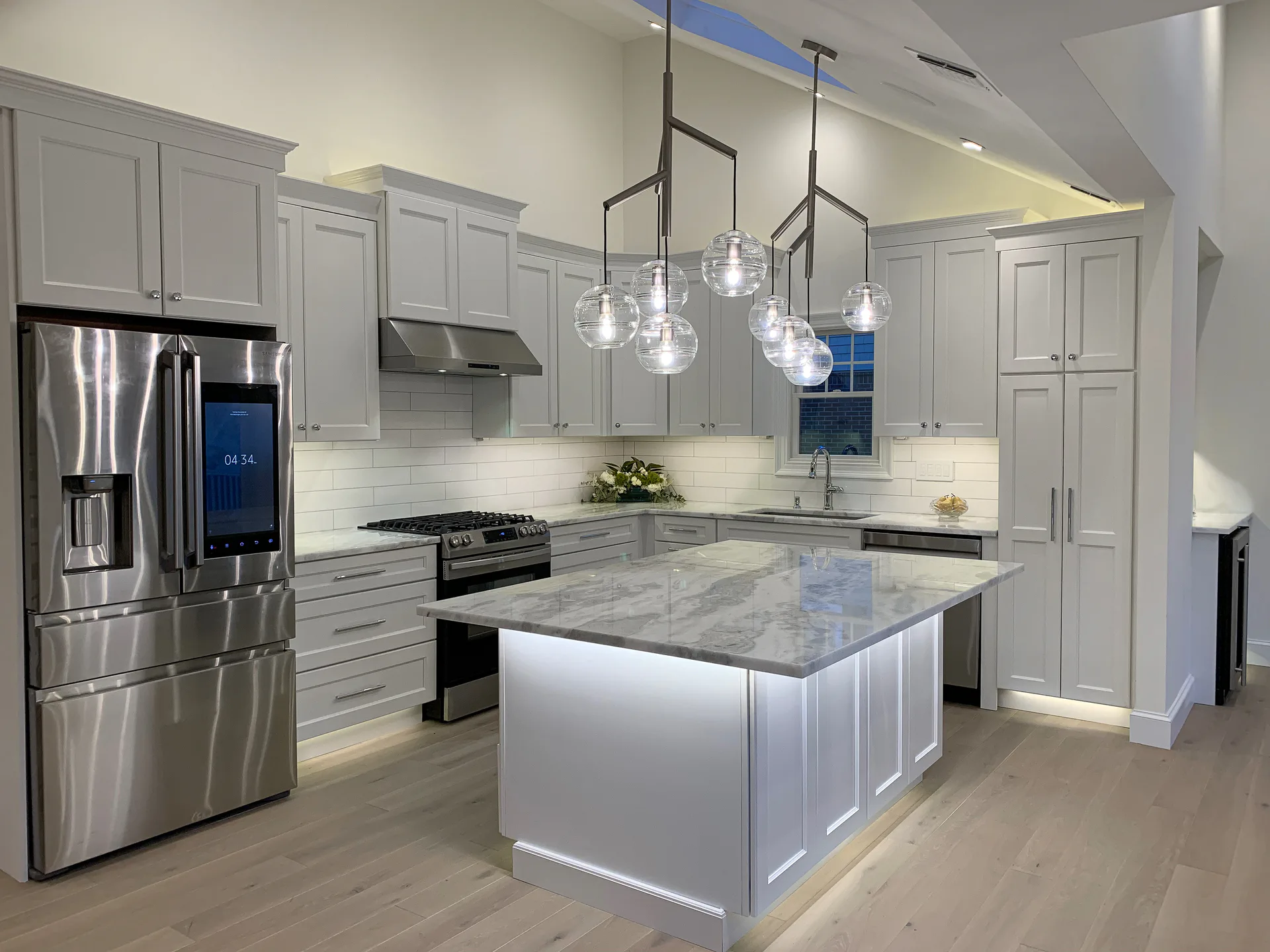 Modern kitchen with gray cabinetry, marble island, stainless steel appliances, and pendant lighting by Christine Ambers.
