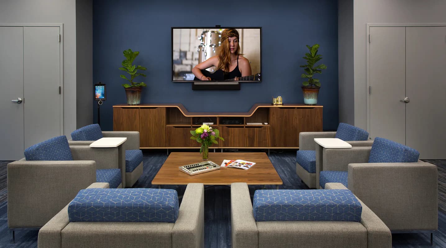 Modern lounge interior with blue accent wall, wood cabinetry, upholstered seating, and mounted TV, designed by Christine Ambers.