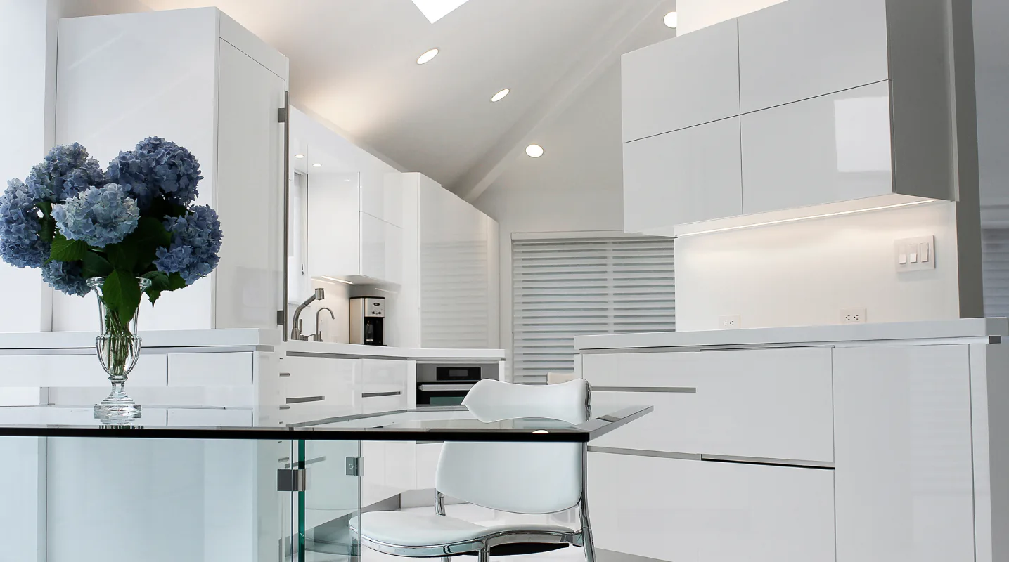 Modern white kitchen with sleek cabinetry, marble countertop, blue hydrangea arrangement, and recessed lighting by Christine Ambers.