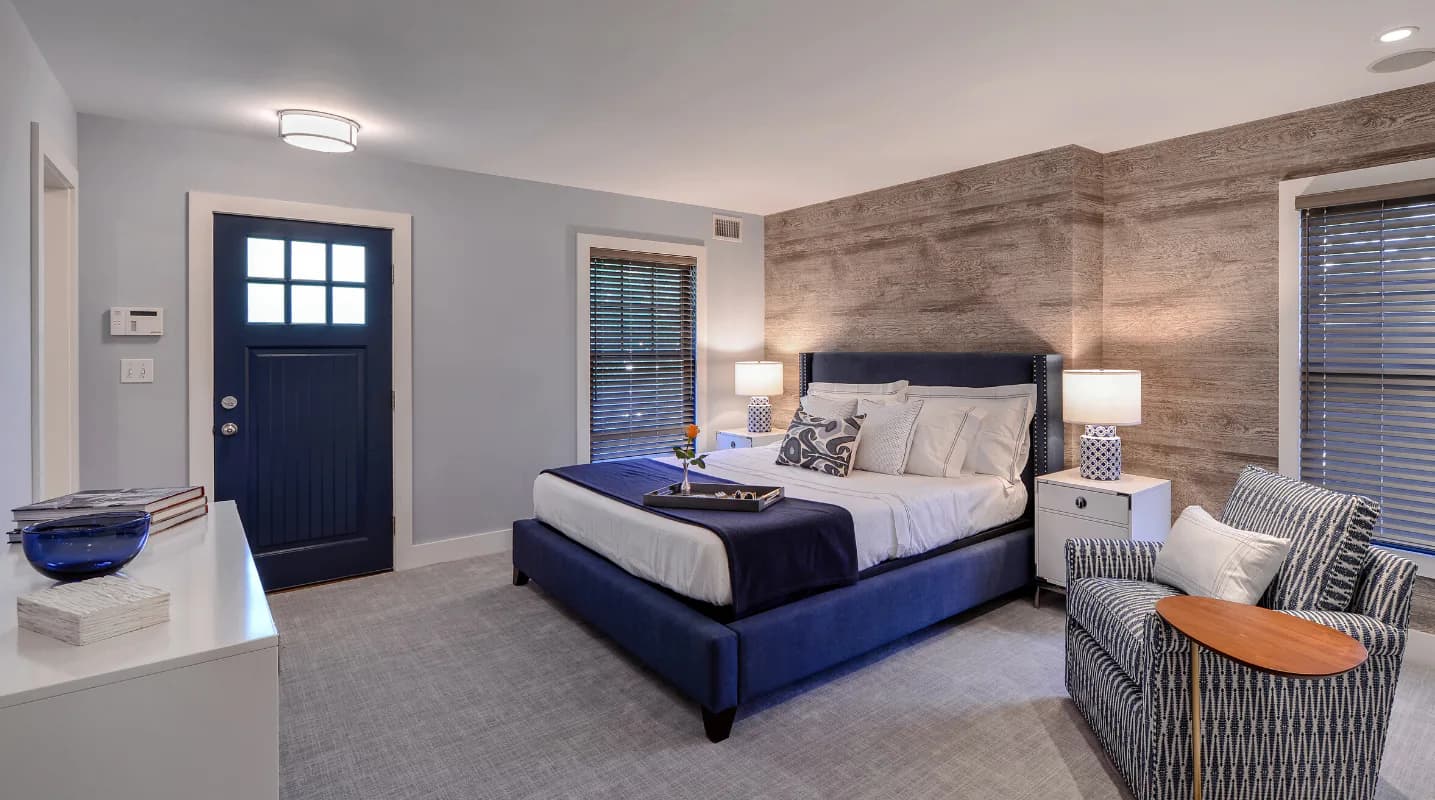 Modern master bedroom with navy upholstered bed, wooden accent wall, gray carpet, and contemporary furnishings by Christine Ambers.