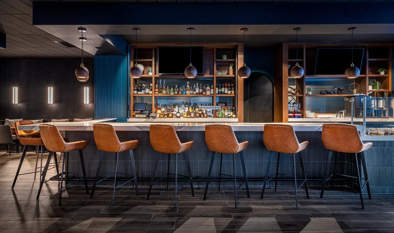 Modern bar interior with navy cabinetry, warm wood accents, and six cognac leather bar stools by Christine Anneken.