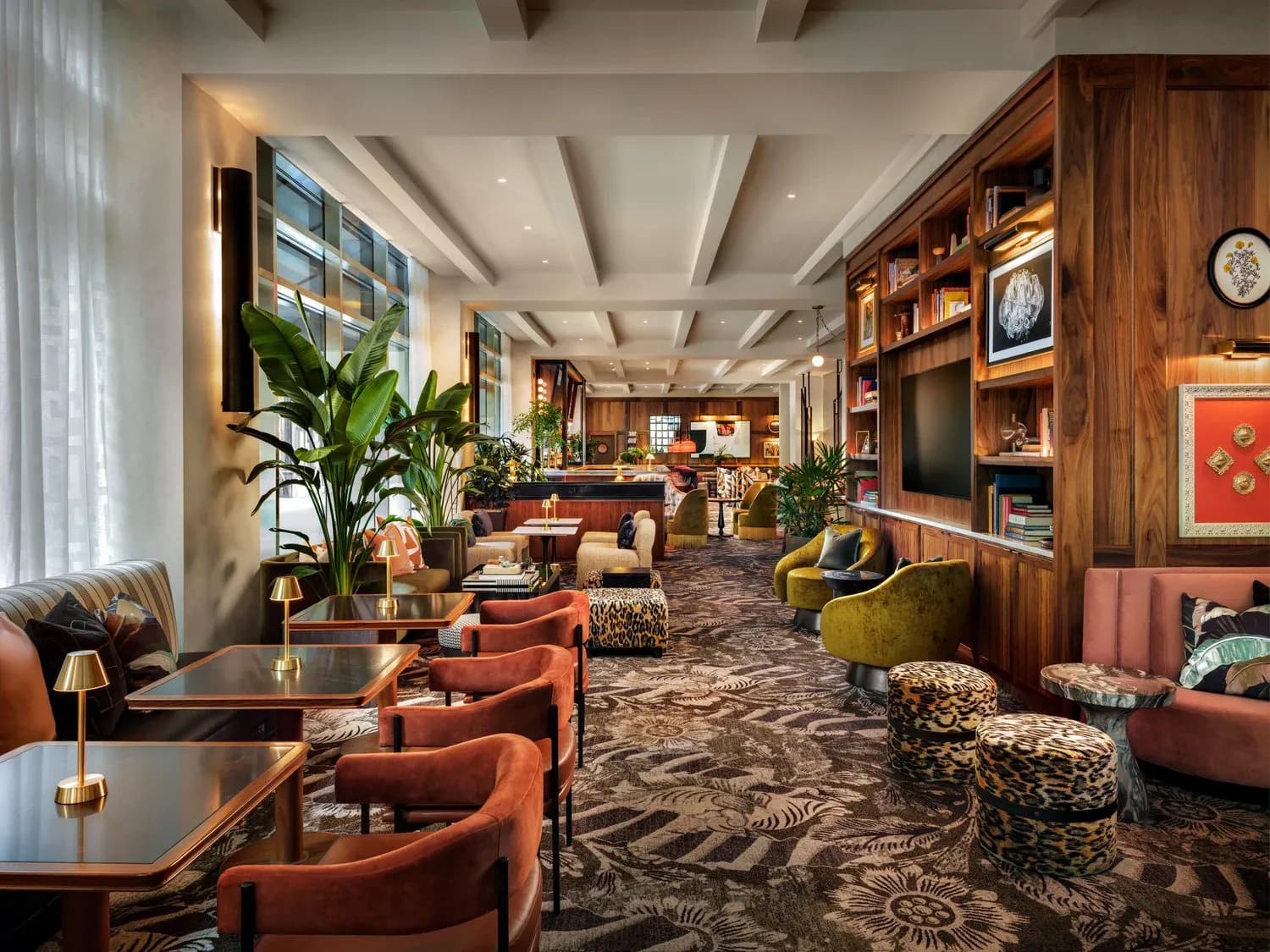 Luxurious hotel lobby lounge with warm terracotta and rust furnishings, rich wood paneling, potted plants, patterned carpet, and coffered ceiling by Christine Anneken.