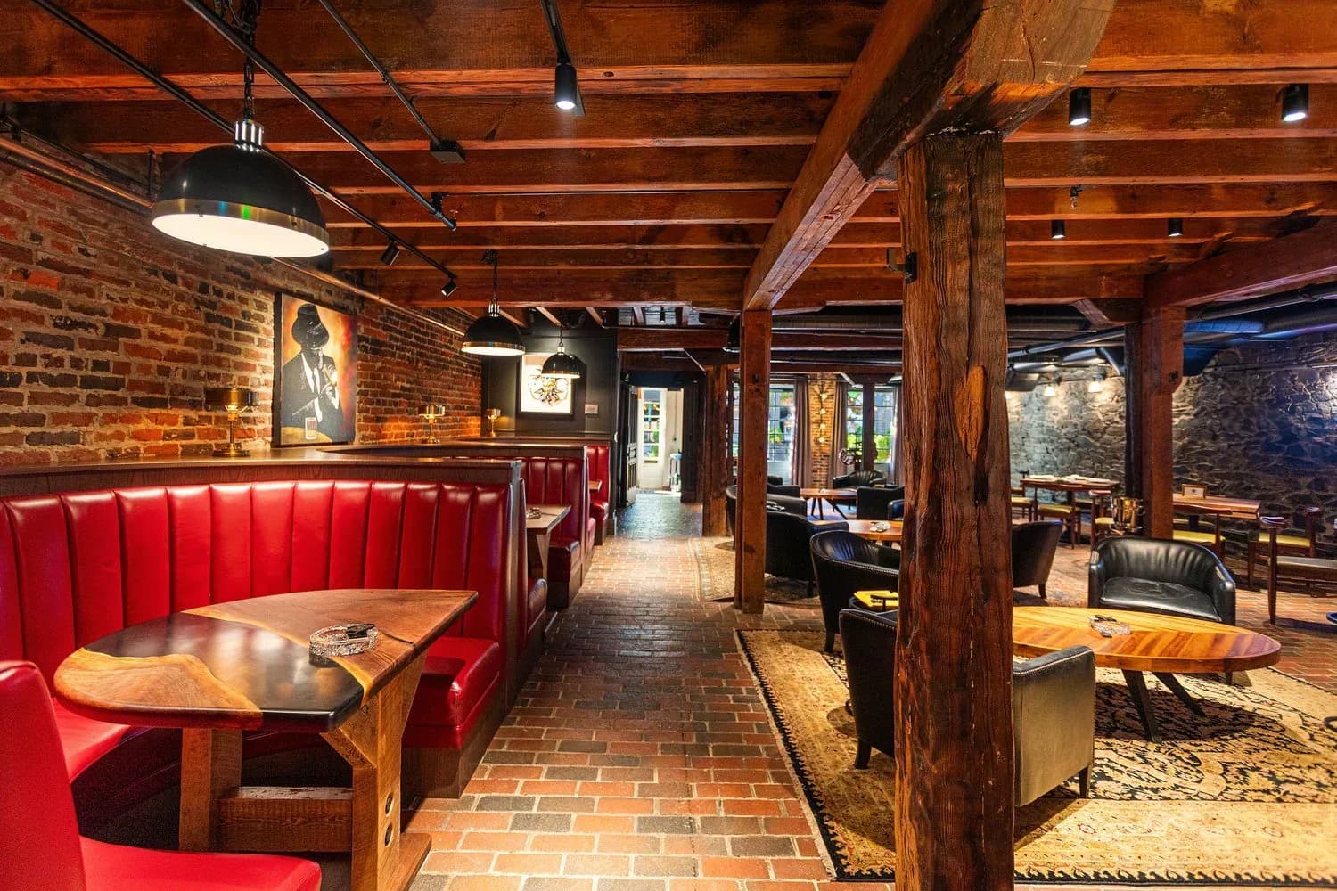 A warm brick and wood interior restaurant or bar space with red banquette seating, wooden beams, pendant lighting, and brick walls, designed by Christine Anneken.