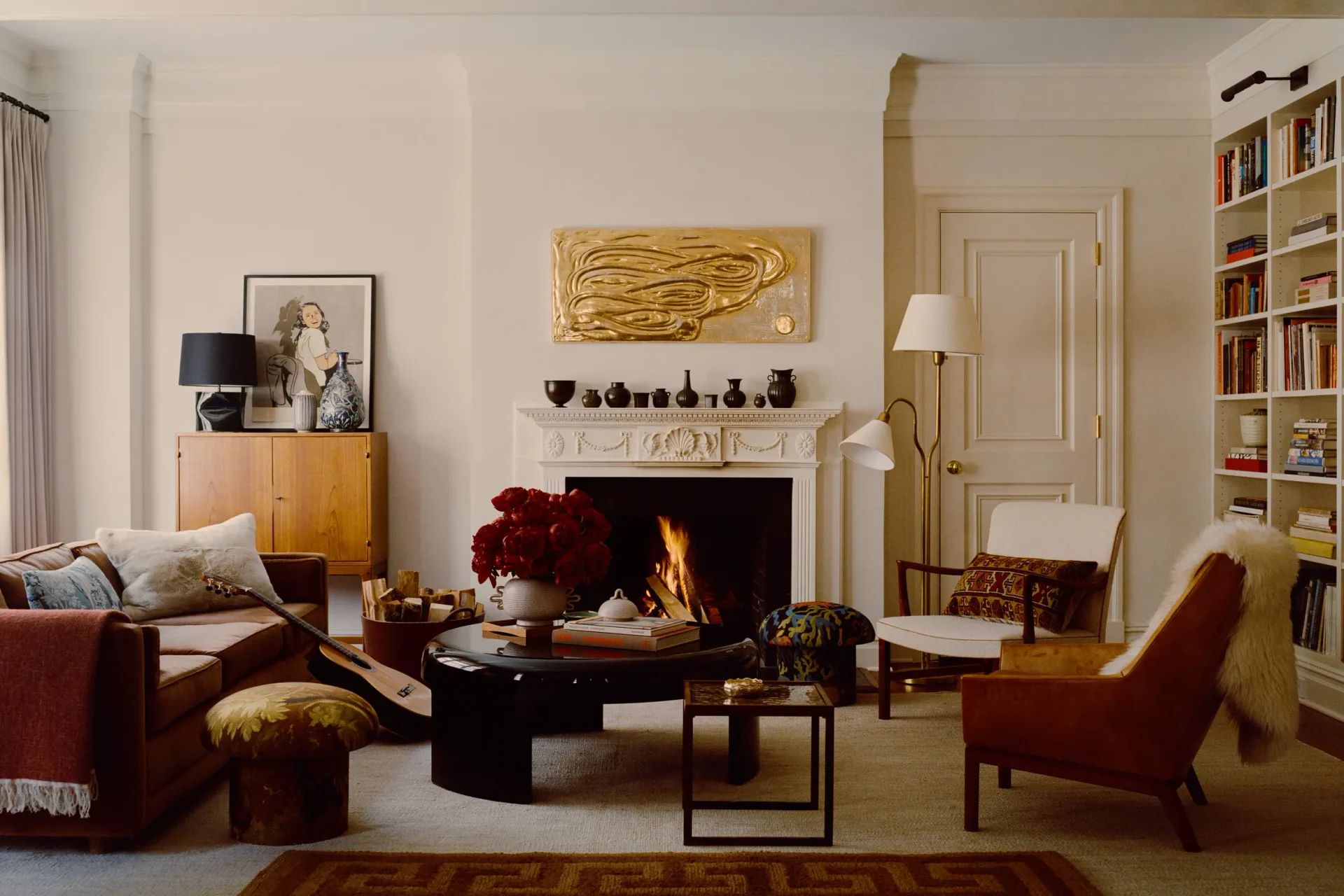 Elegant living room with fireplace, burgundy armchairs, wooden mid-century dresser, built-in bookshelves, and warm neutral palette by Christine Gachot.