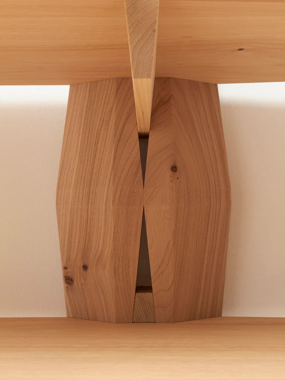Wooden furniture detail showing a sculptural joint with split legs in warm-toned wood, demonstrating refined joinery and craftsmanship by Christophe Delcourt.