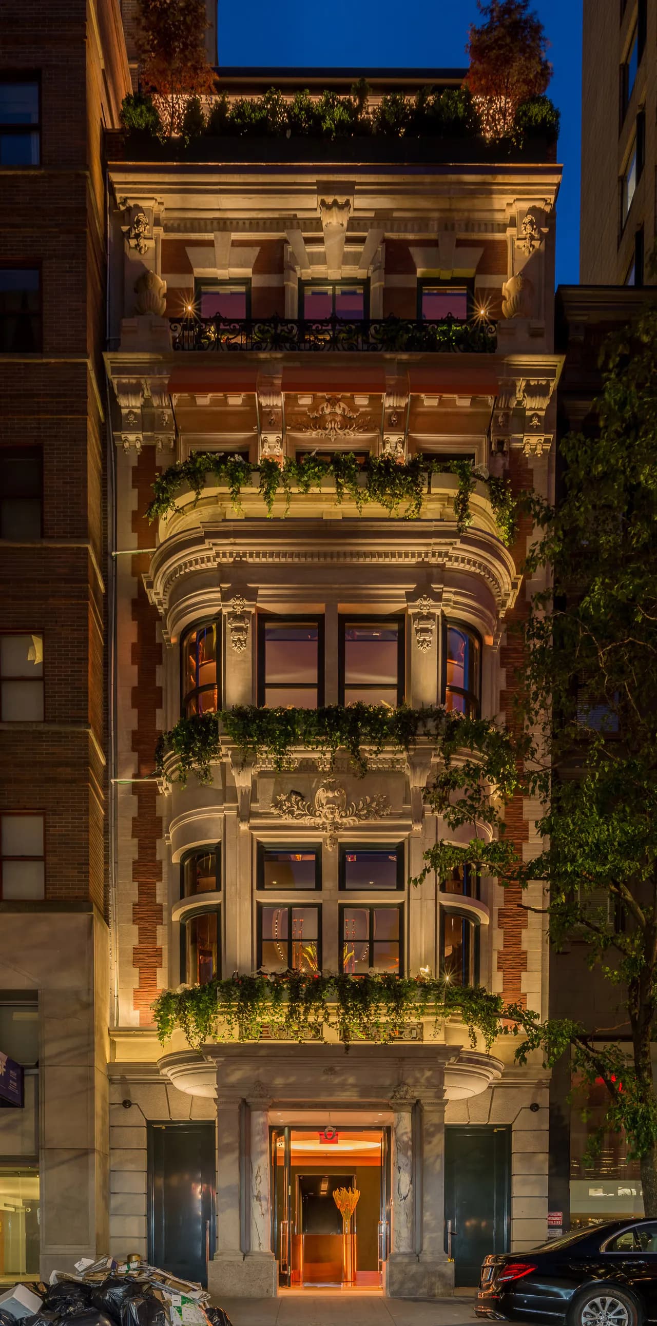 Illuminated historic townhouse facade at dusk featuring ornate classical stone details, decorative balconies with planters, and warm accent lighting by Christopher Cheap.