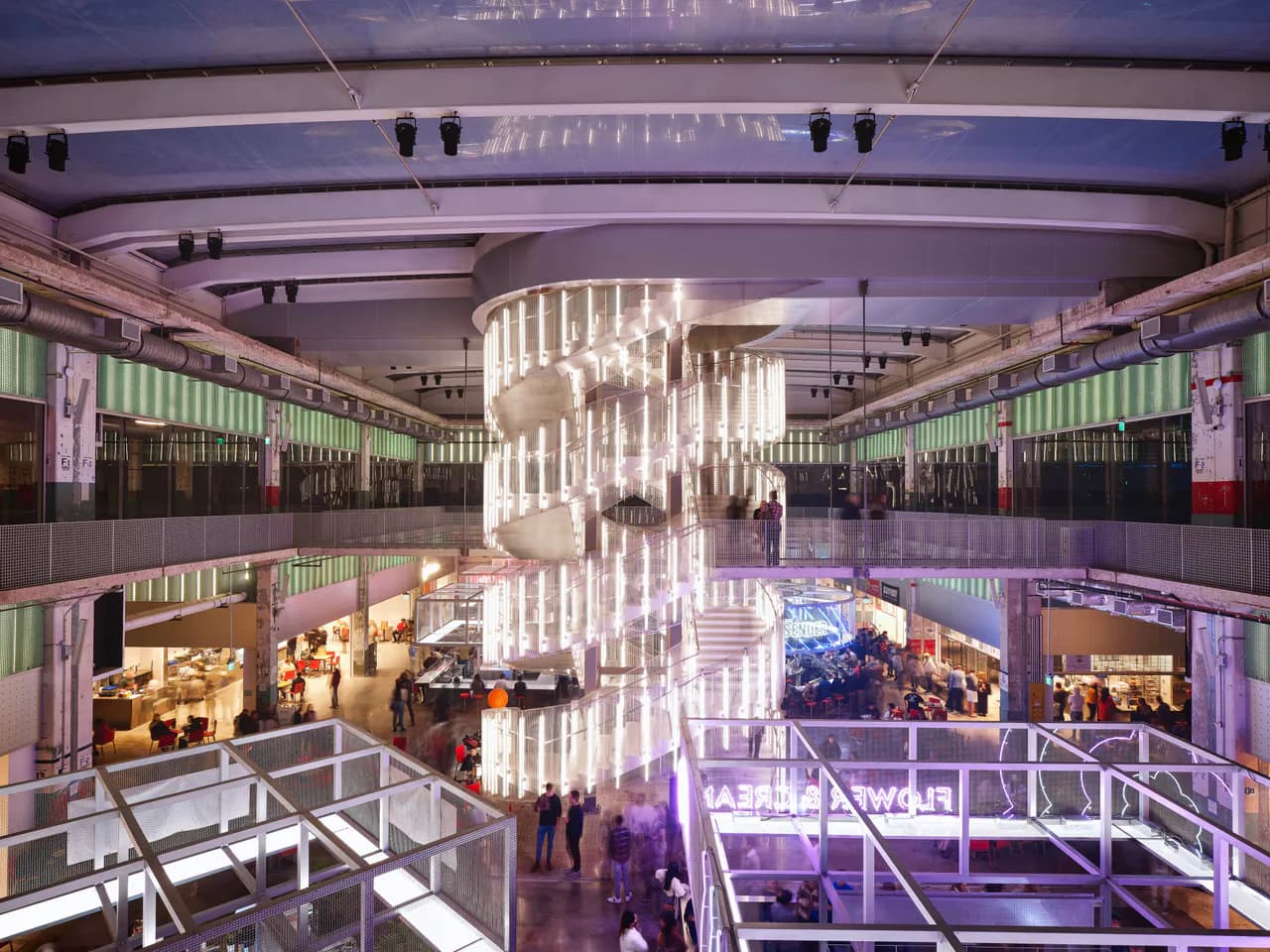 Multi-level modern shopping mall interior with striking white sculptural chandelier, purple ambient lighting, and green-paneled storefronts by Christopher Cheap.