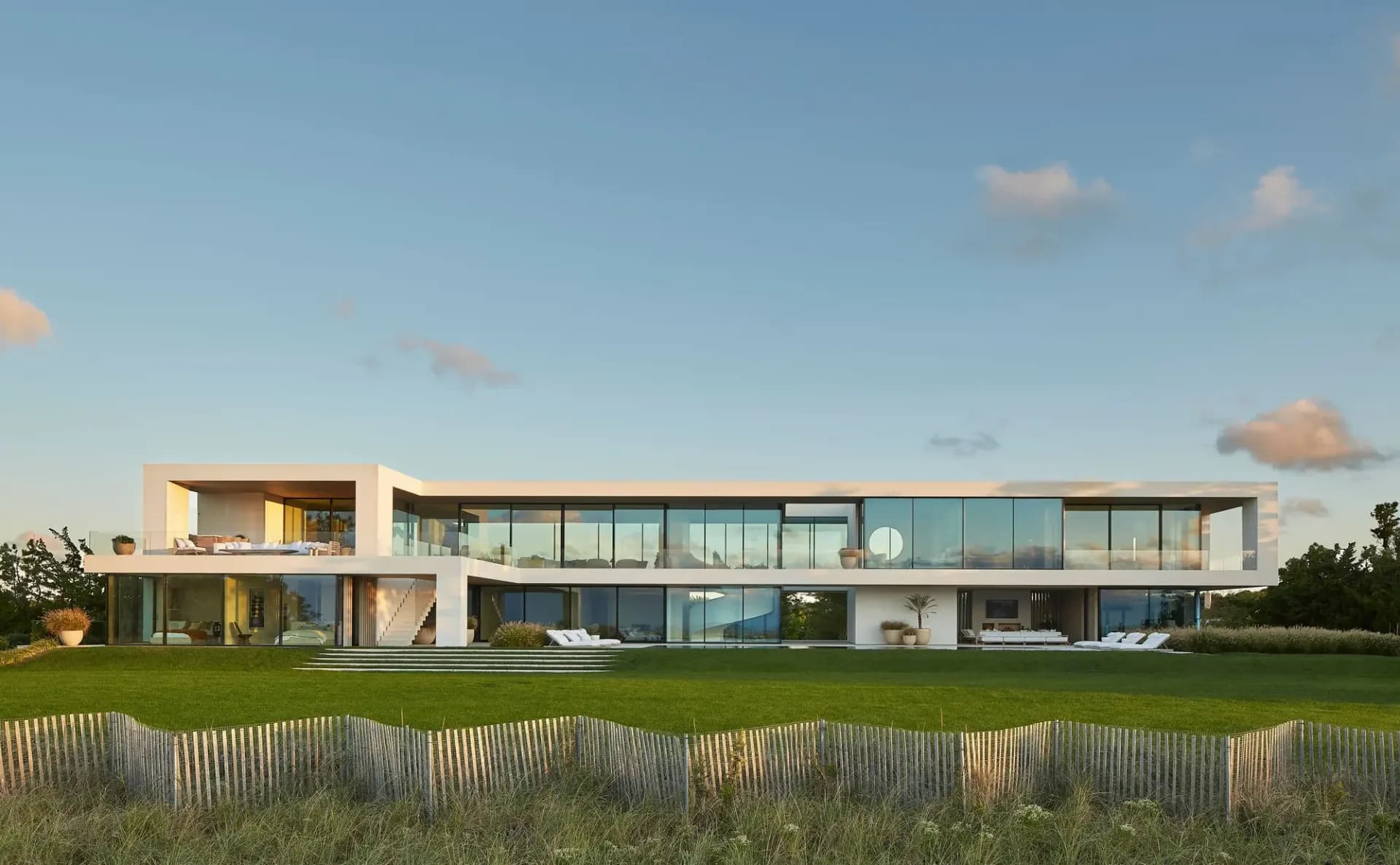 Modern horizontal residence with glass and cream facades overlooking manicured lawn and dune fencing by Christopher Coy.