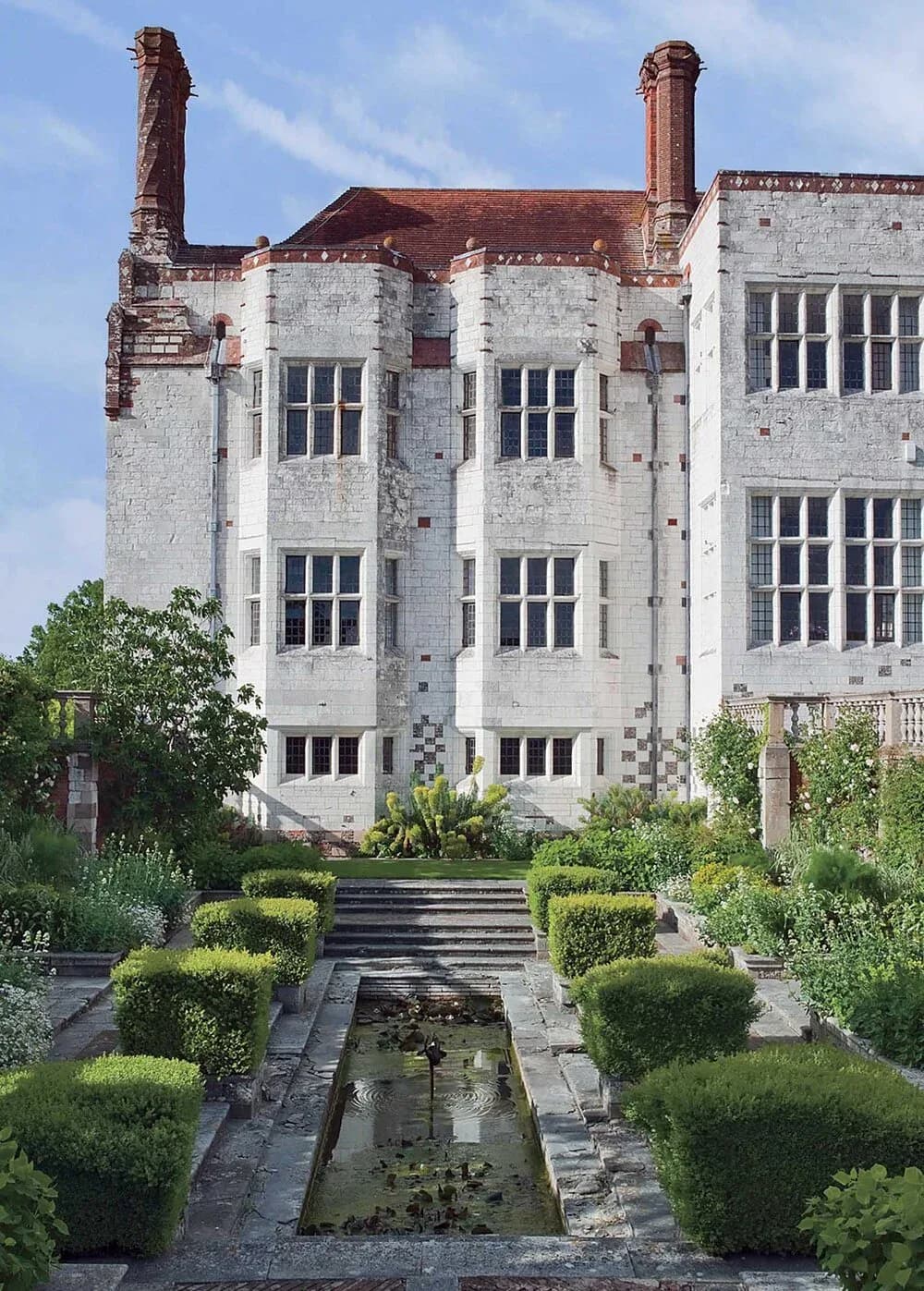 Whitewashed brick building with red chimneys and multi-pane windows overlooking a formal garden with reflecting pool and manicured hedges by Christopher Labrot.