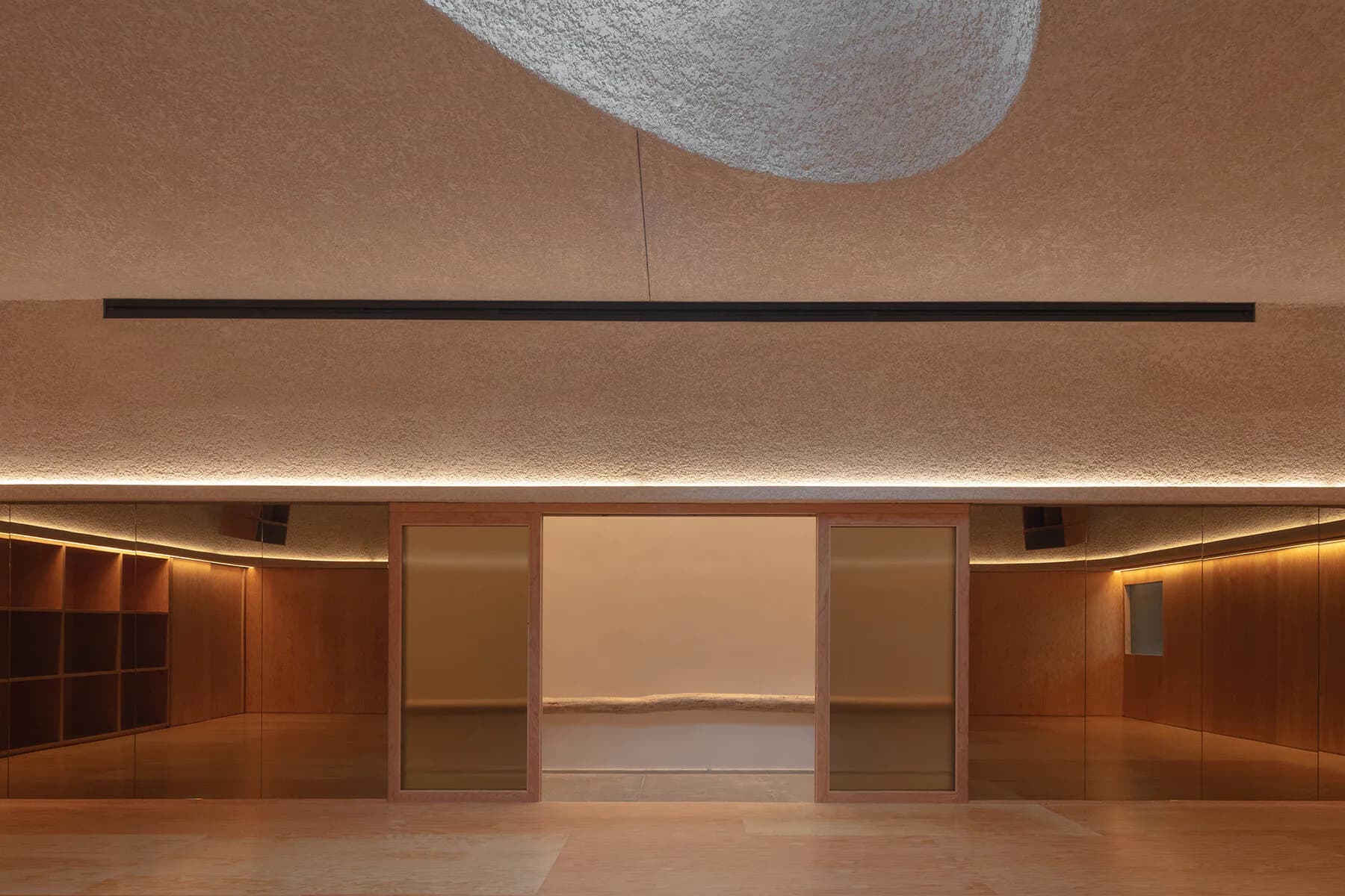 Minimalist gallery space with warm wood paneling, ambient lighting, and central illuminated wall by Christopher Leong.