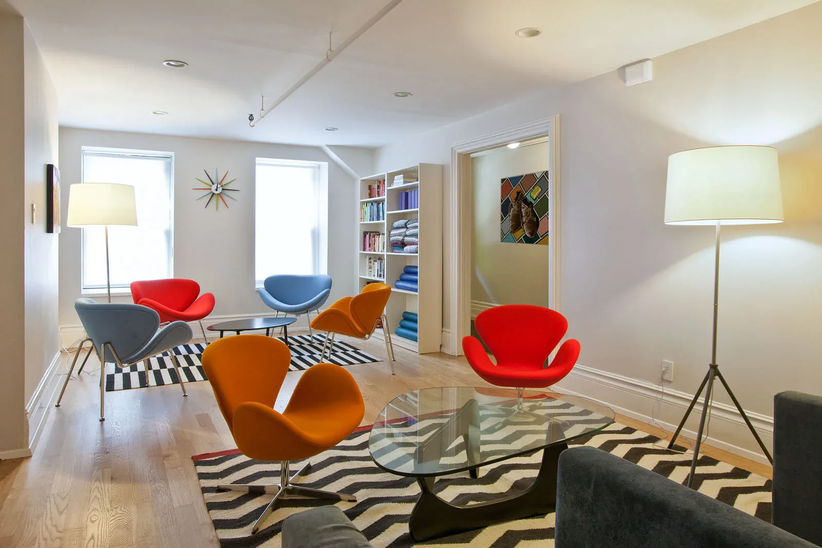 Modern lounge with colorful molded chairs, geometric patterned rugs, built-in shelving, and contemporary lighting designed by Christopher Scholz.