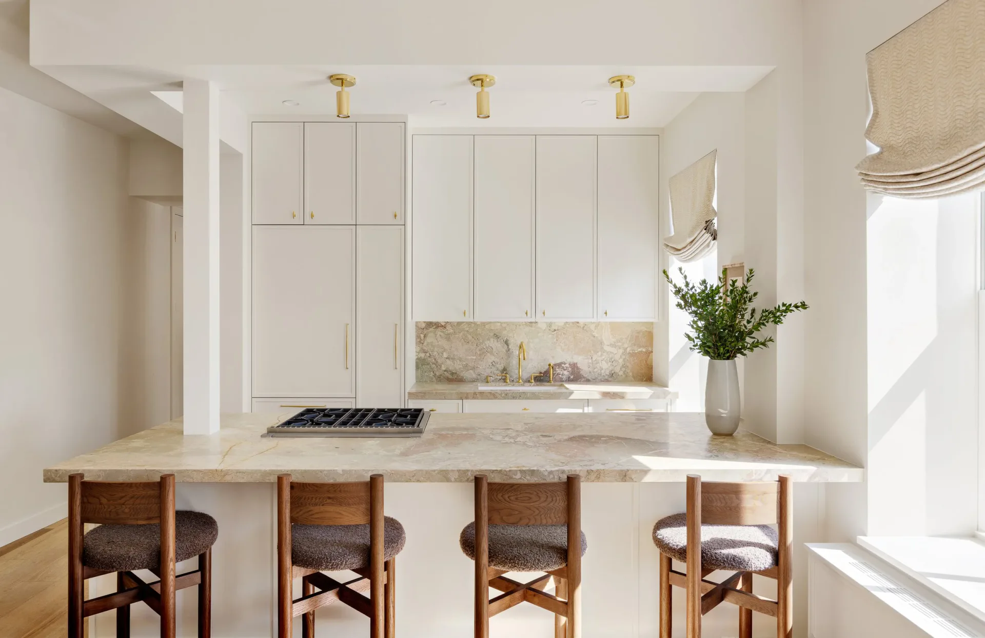 Minimalist kitchen with white cabinetry, marble countertop island, wooden bar stools, and brass pendant lights by Christopher Sondi.