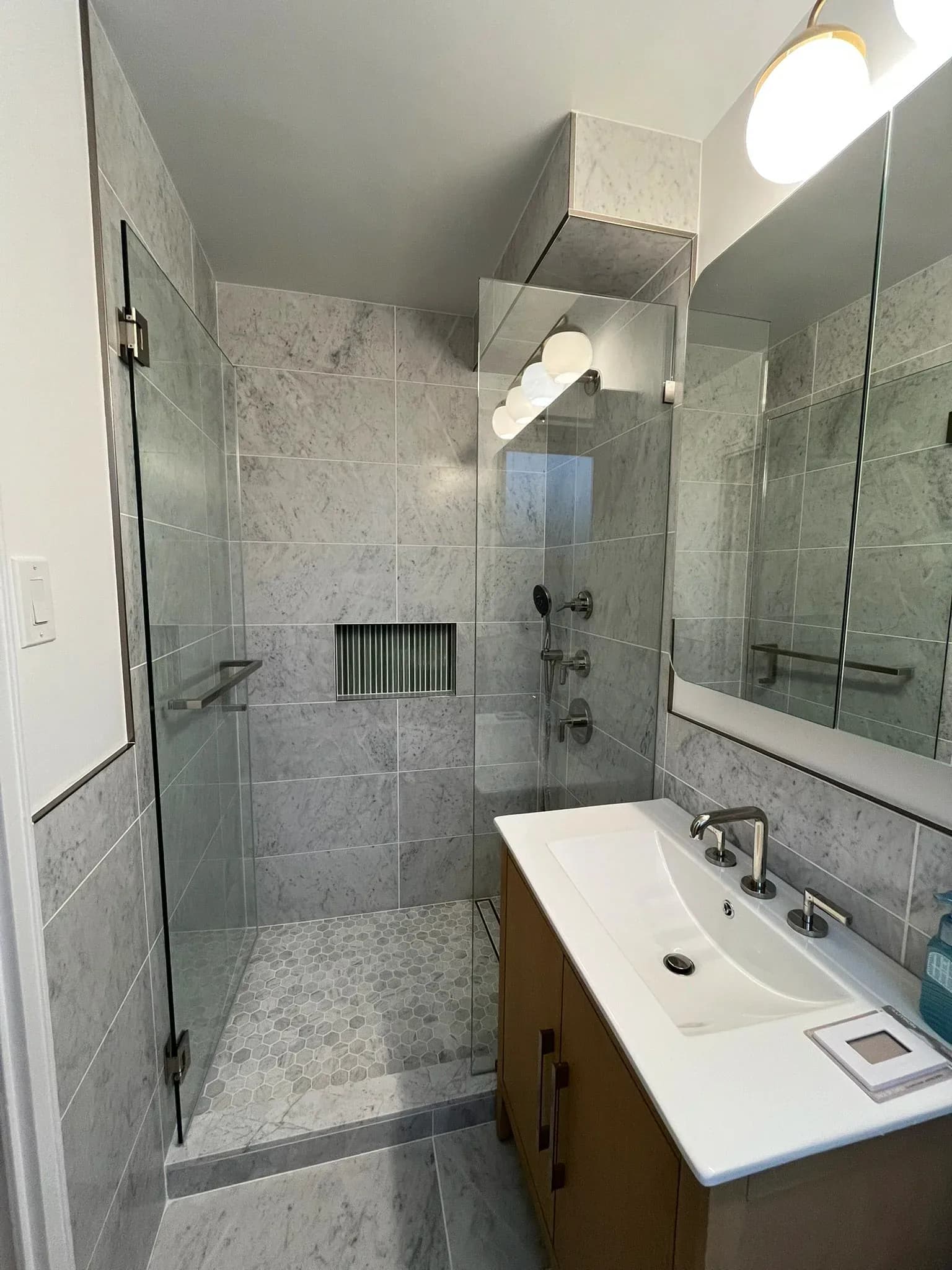Modern bathroom with marble tile shower enclosure, floating vanity with white countertop, and polished finishes by Christopher Sondi.