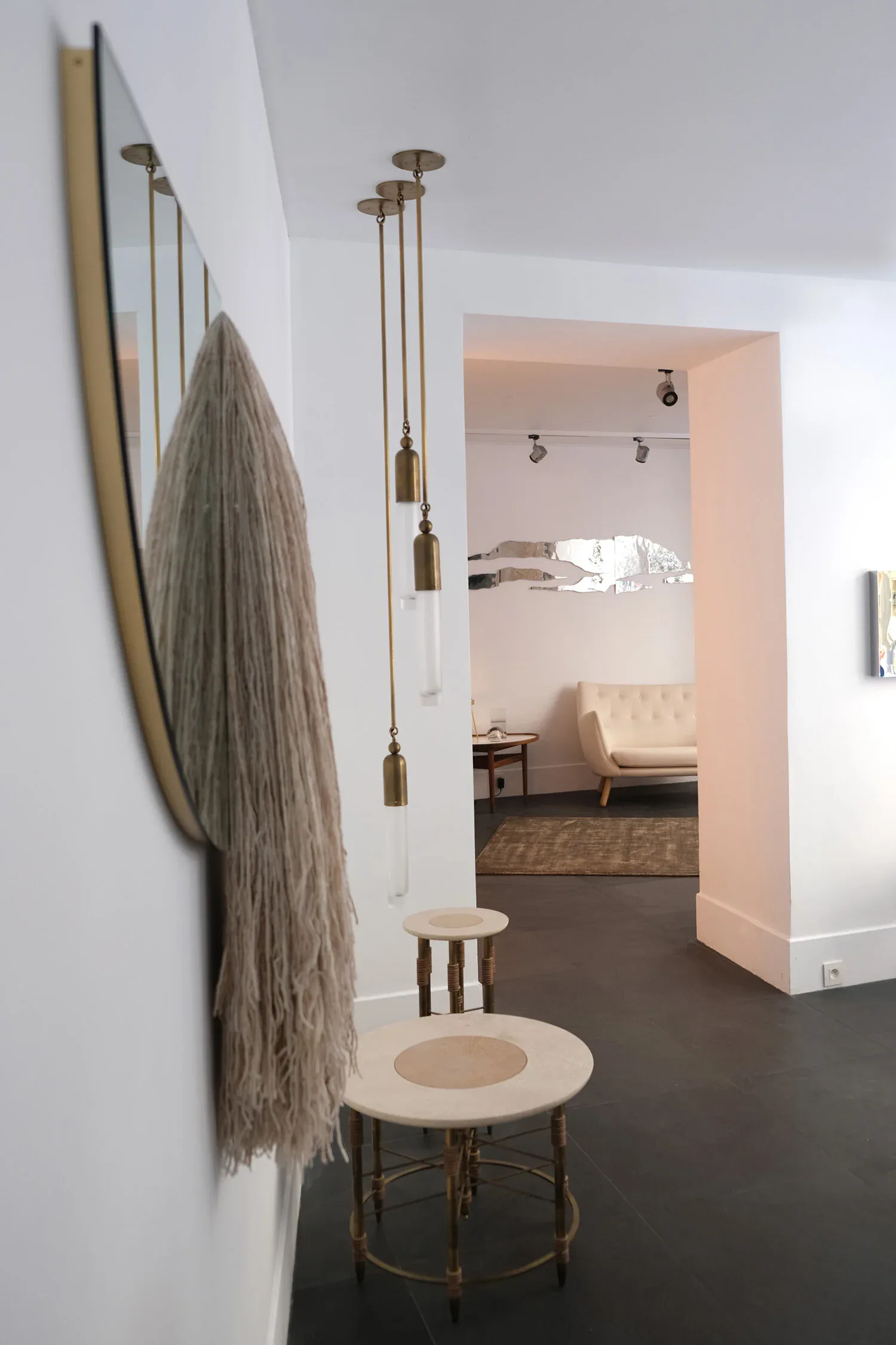 Modern interior with gray textile hanging, brass pendant lights, and round side tables in a minimalist gallery space by Christopher Stuart.