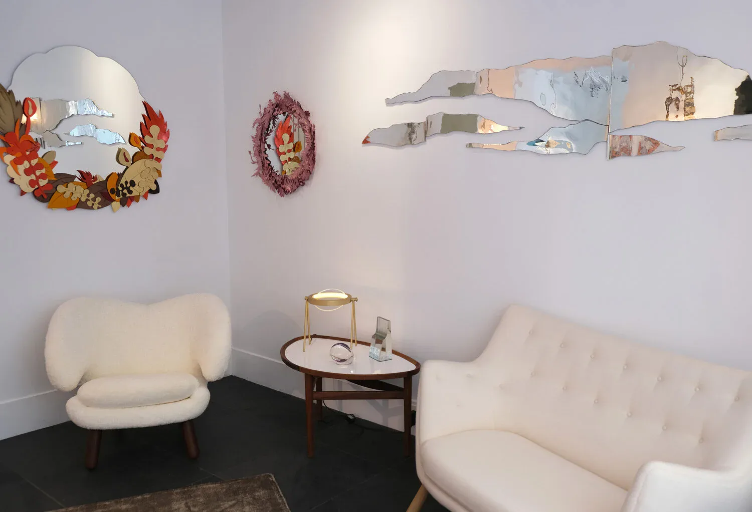 Modern lounge space with cream curved seating, decorative floral wreaths, floating shelves, and mid-century side table by Christopher Stuart.