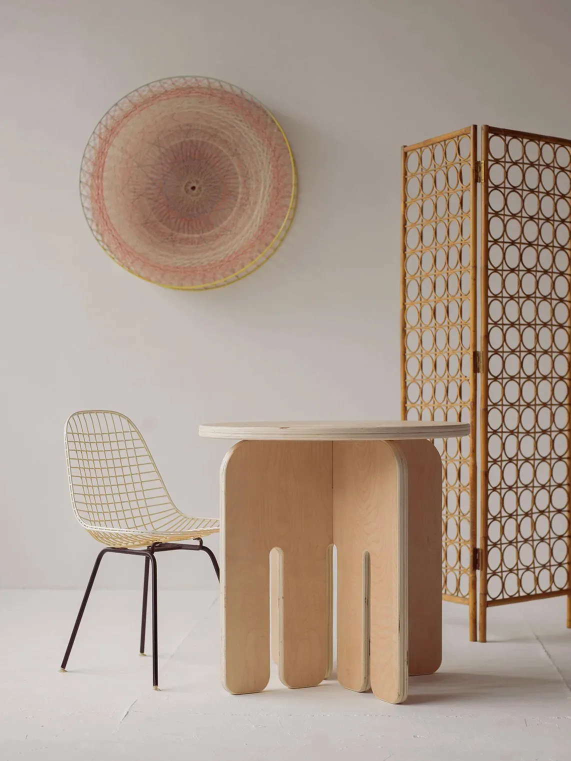 Minimalist studio setting with cardboard furniture, woven chair, circular wall installation, and decorative room divider by Ciara Dockery.